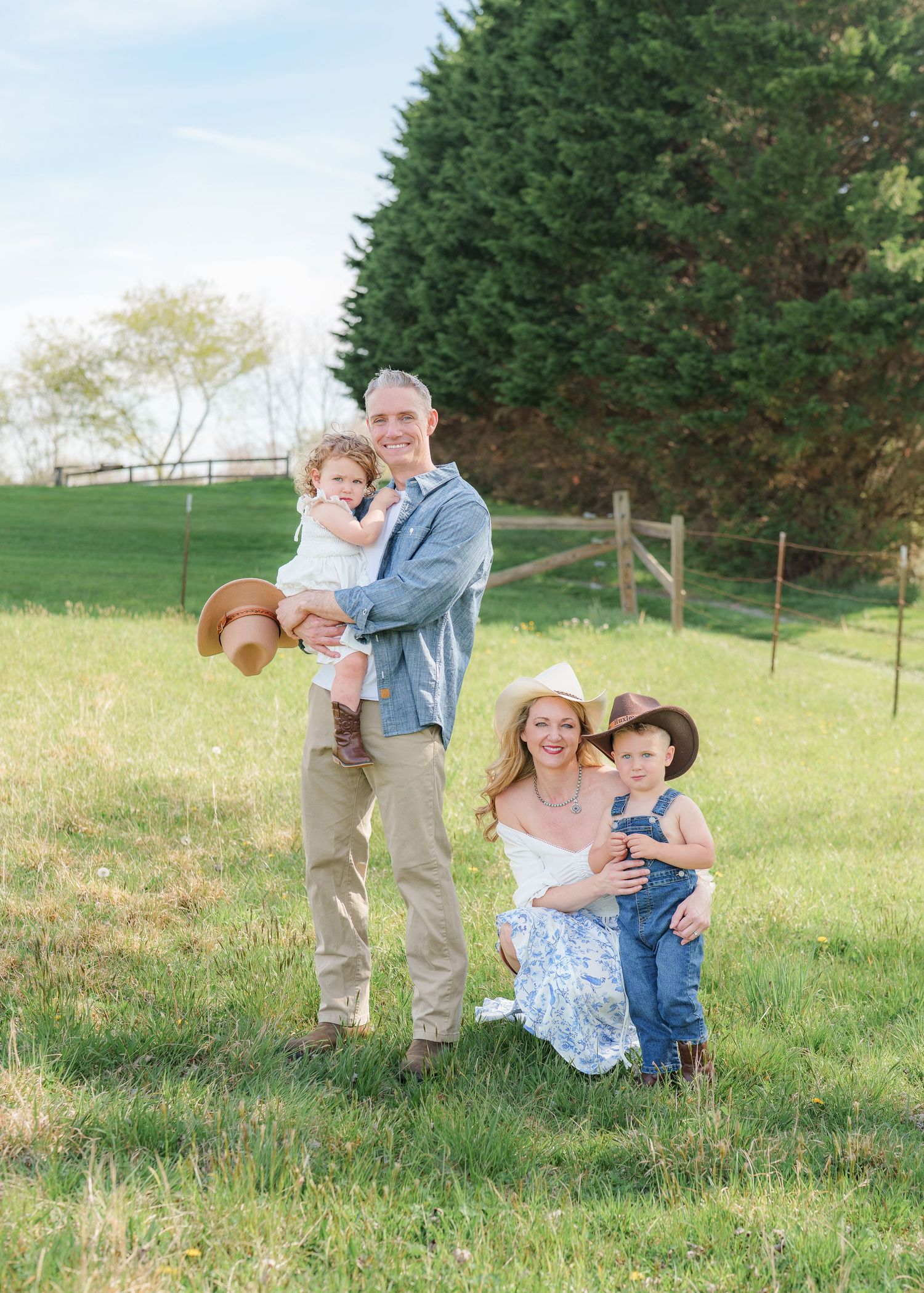 Family of four posing in green meadow wearing cowboy hats and denim outfits on spring day.