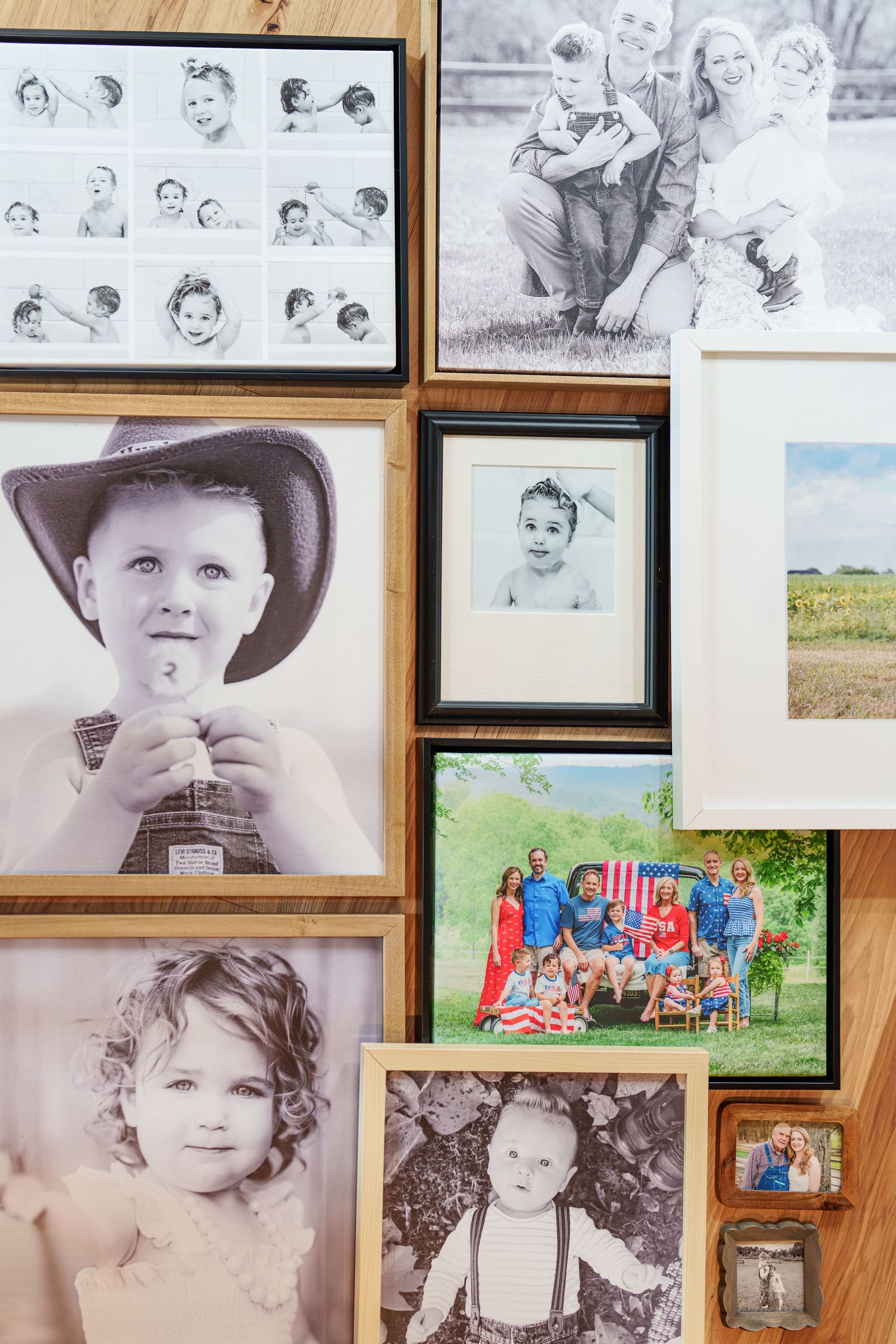 A wooden wall gallery display featuring black and white and color family portrait photos of children and adults.