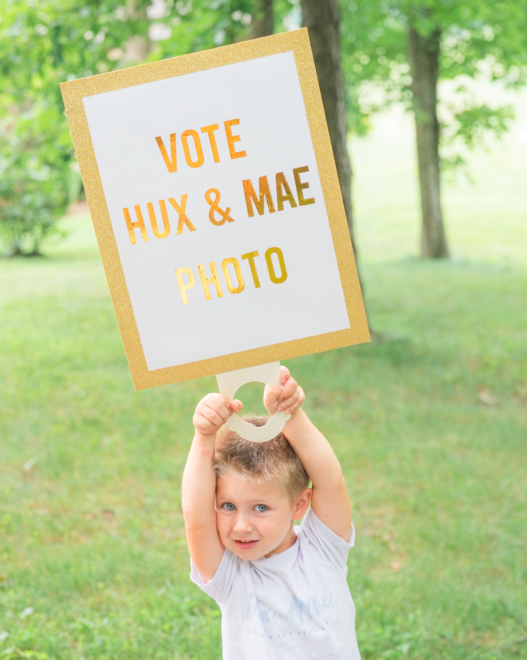 Cute toddler holding a gold-framed sign reading Vote Hux and Mae Photo outdoors.