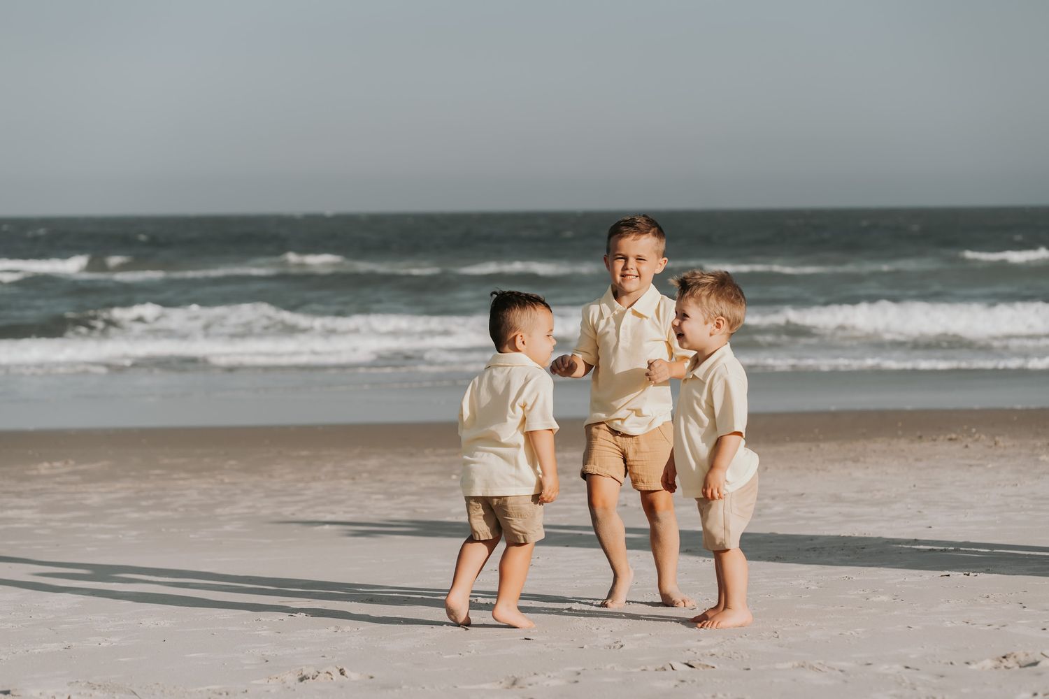 Three young boys in matching outfits playing together on a sandy beach.