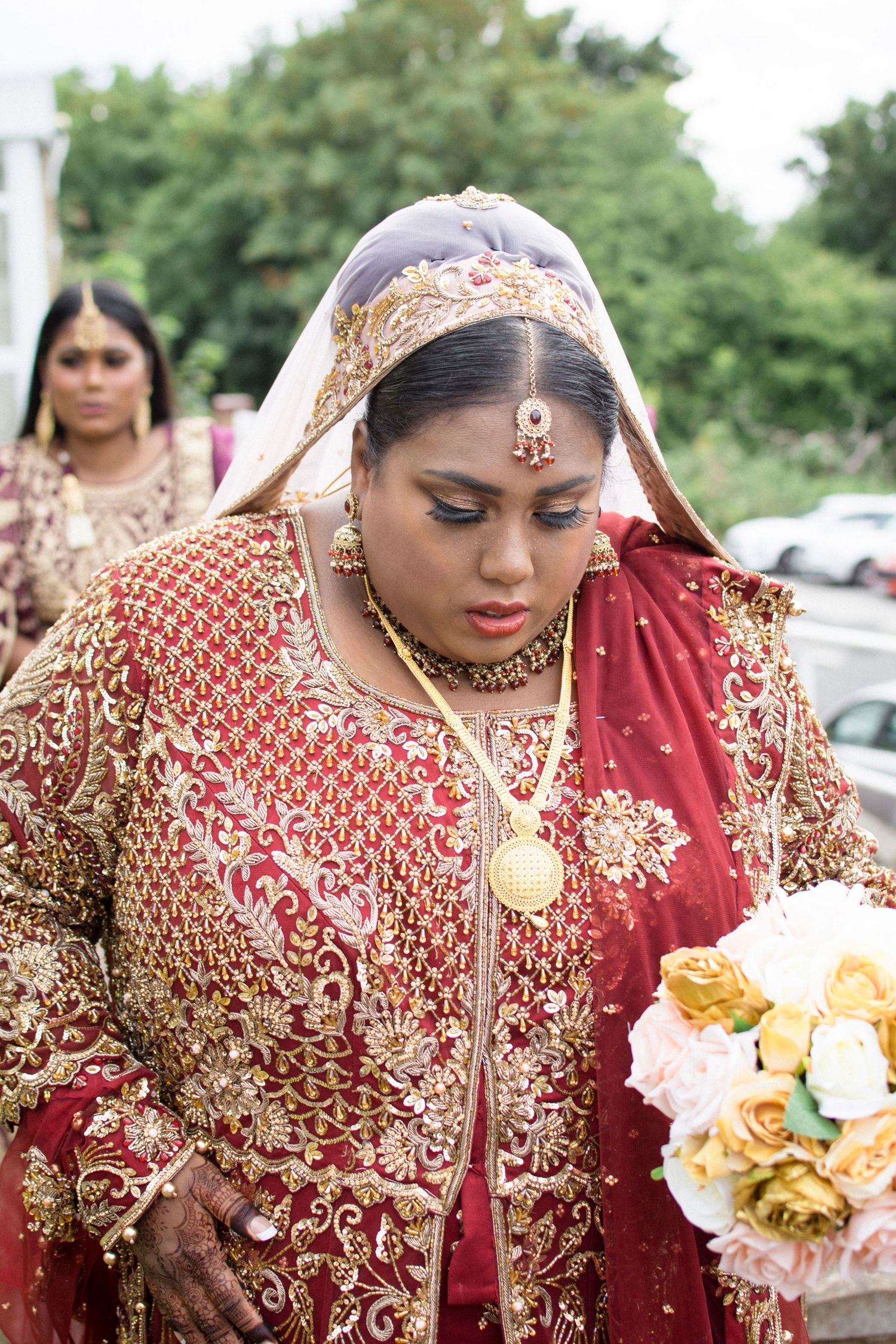 Traditional Indian bridal attire in deep red with gold embroidery and floral bouquets.