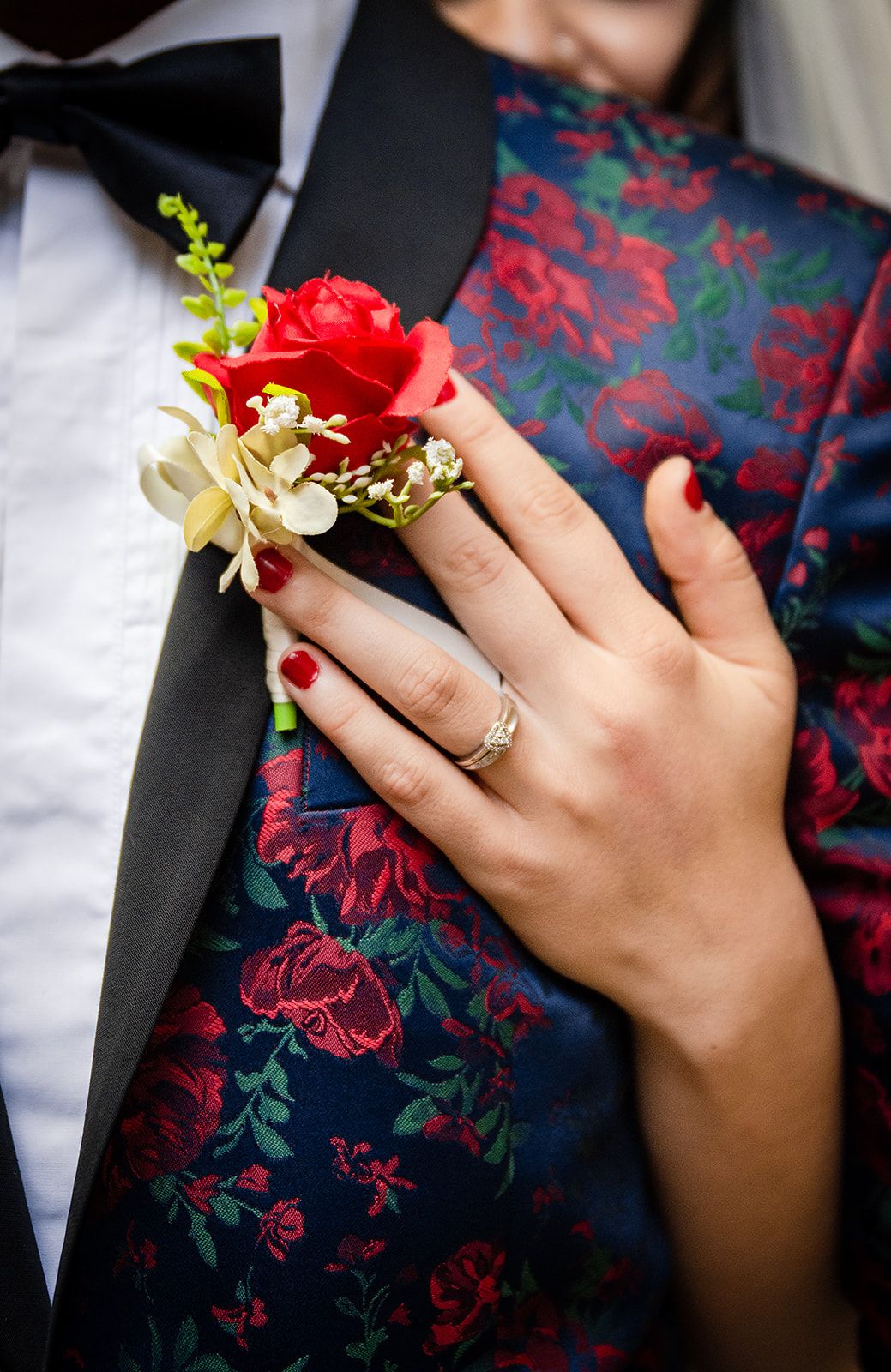 Hands wearing wedding rings shown against a floral patterned dress with red and navy details.