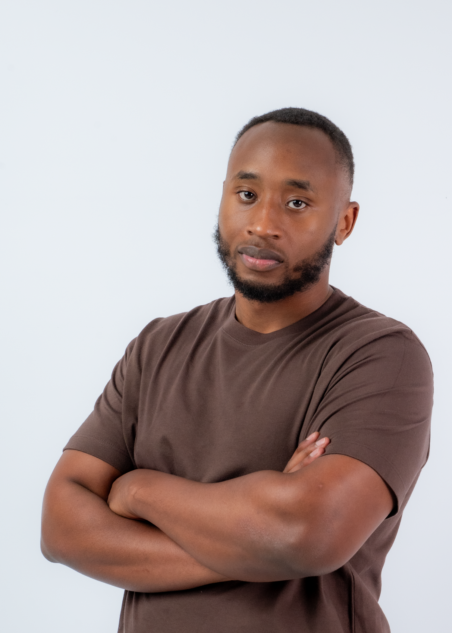 Professional studio portrait of a person in a brown t-shirt against white background.