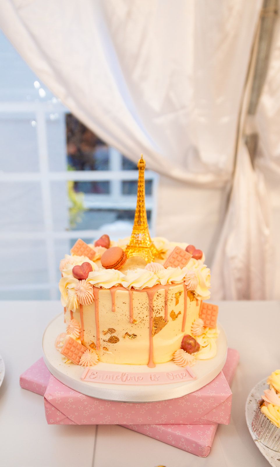 Paris-themed celebration cake with gold Eiffel Tower topper and pink accents.