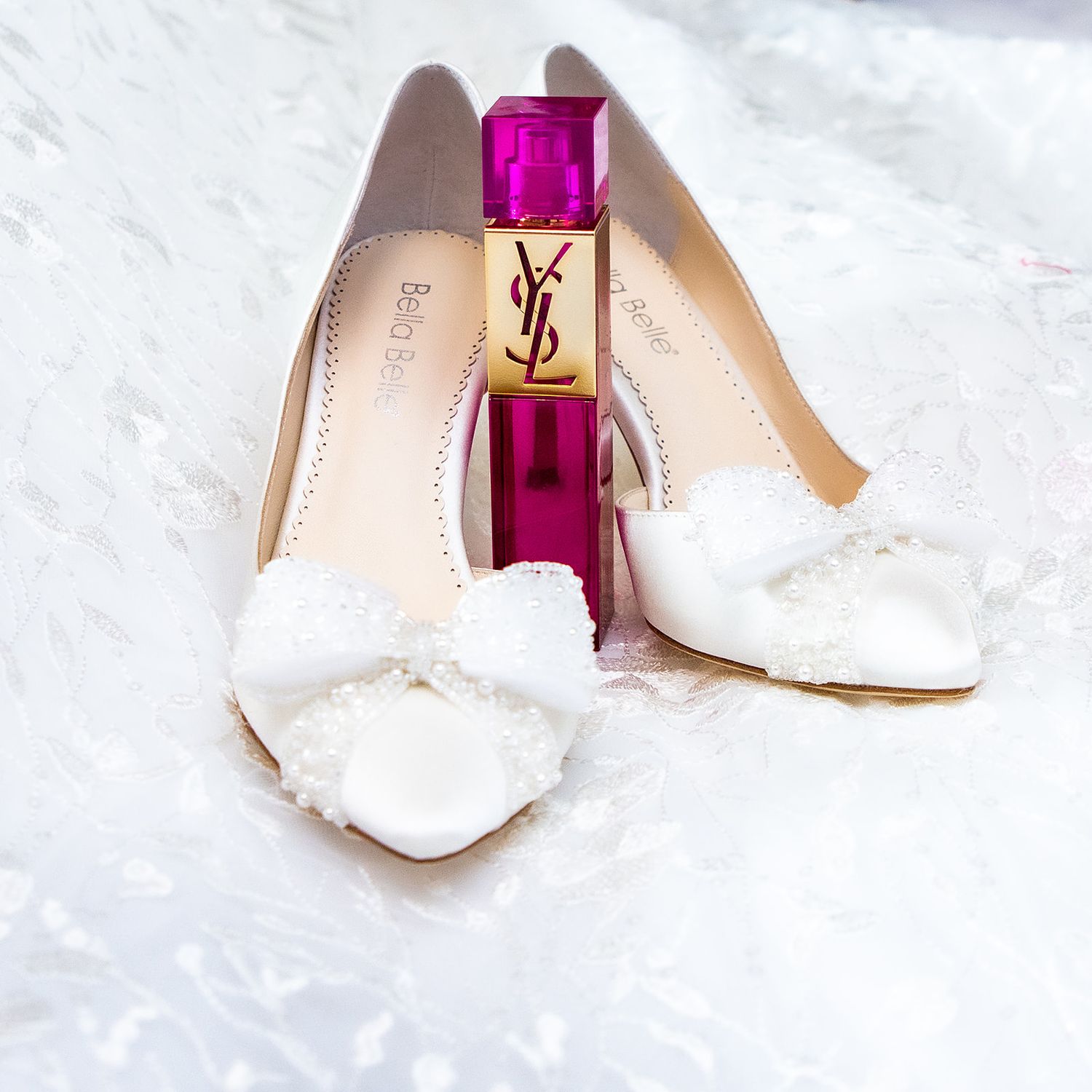 Elegant bridal shoes and perfume arranged on white fabric.