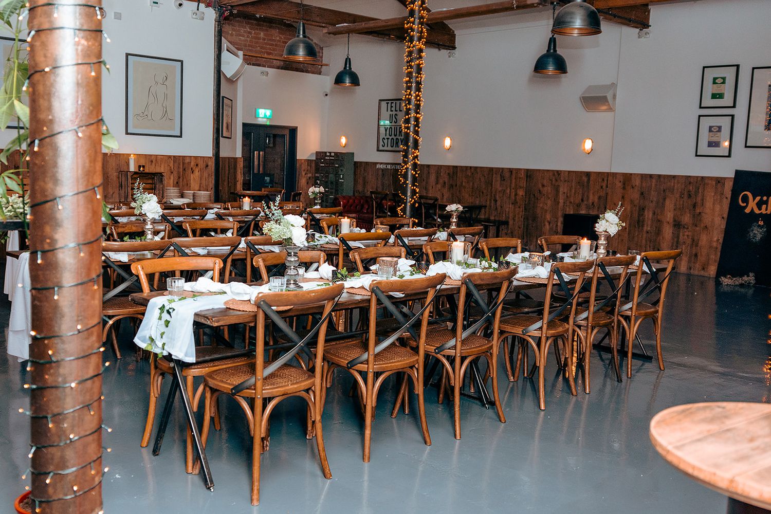 Reception venue interior with wooden crossback chairs and rustic columns.