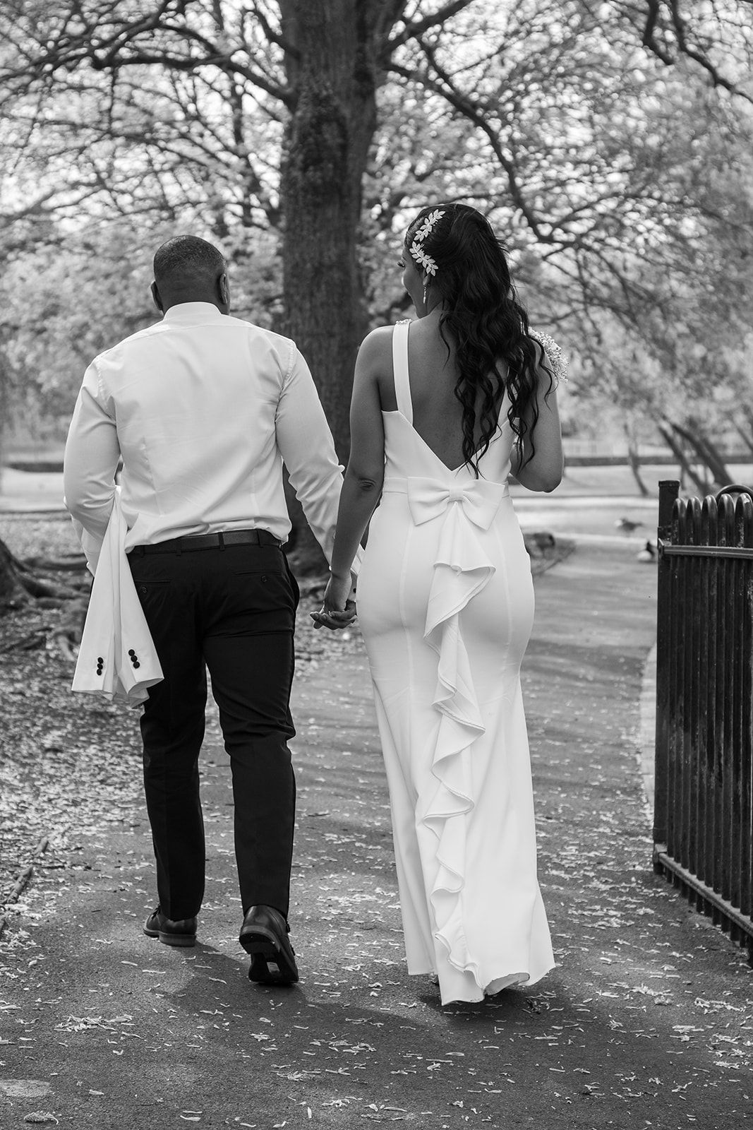 A black and white wedding photo of a couple walking hand in hand along a tree-lined path.