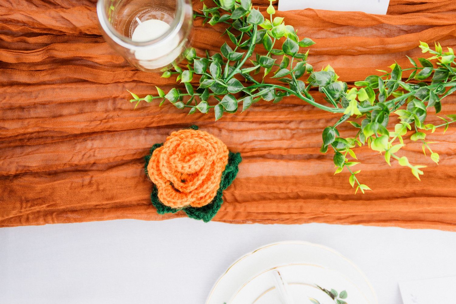 Rustic table decor featuring orange roses and greenery on wooden surface.