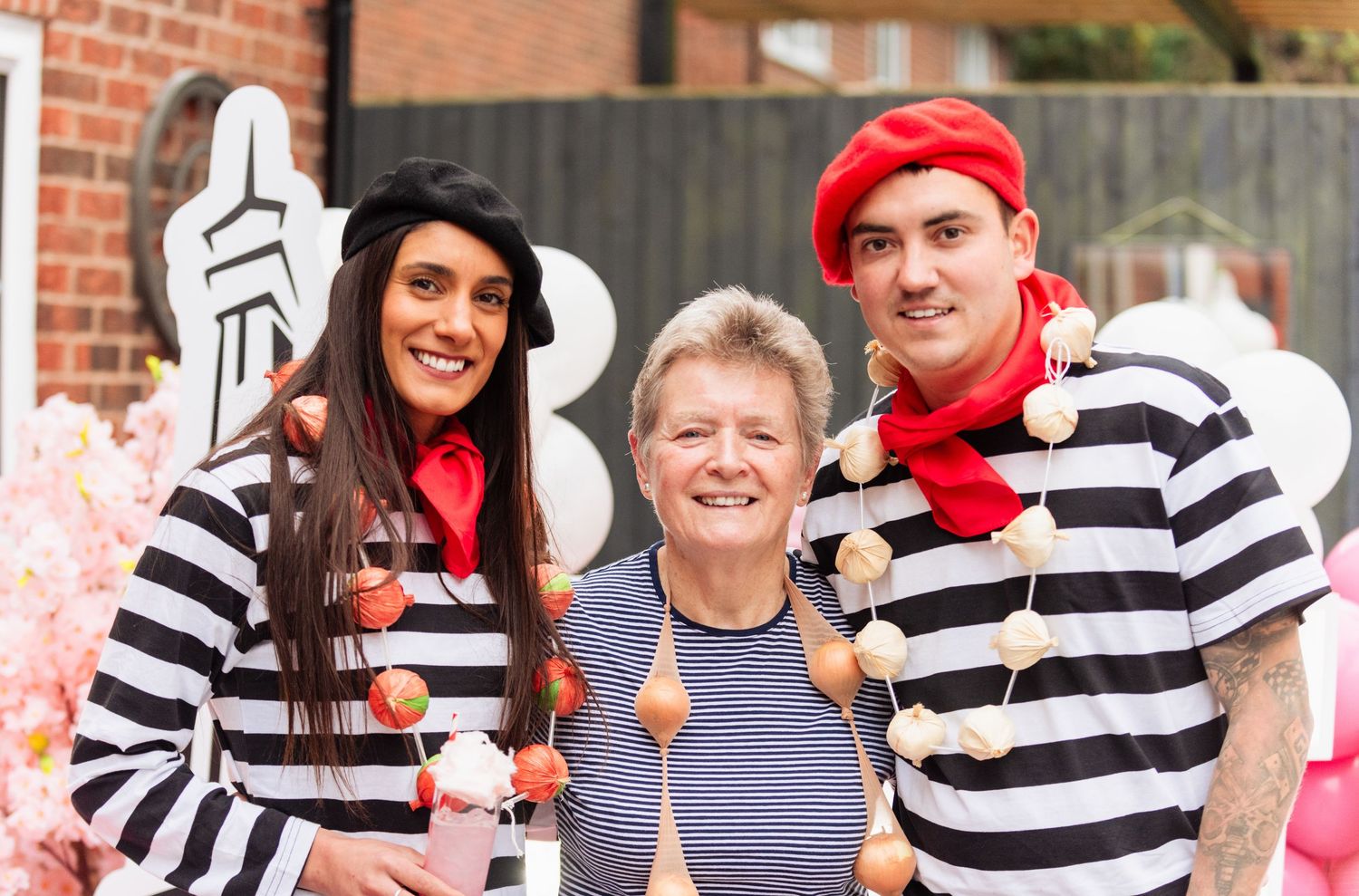 Group wearing striped shirts posing together at festive party with pink balloon decorations.