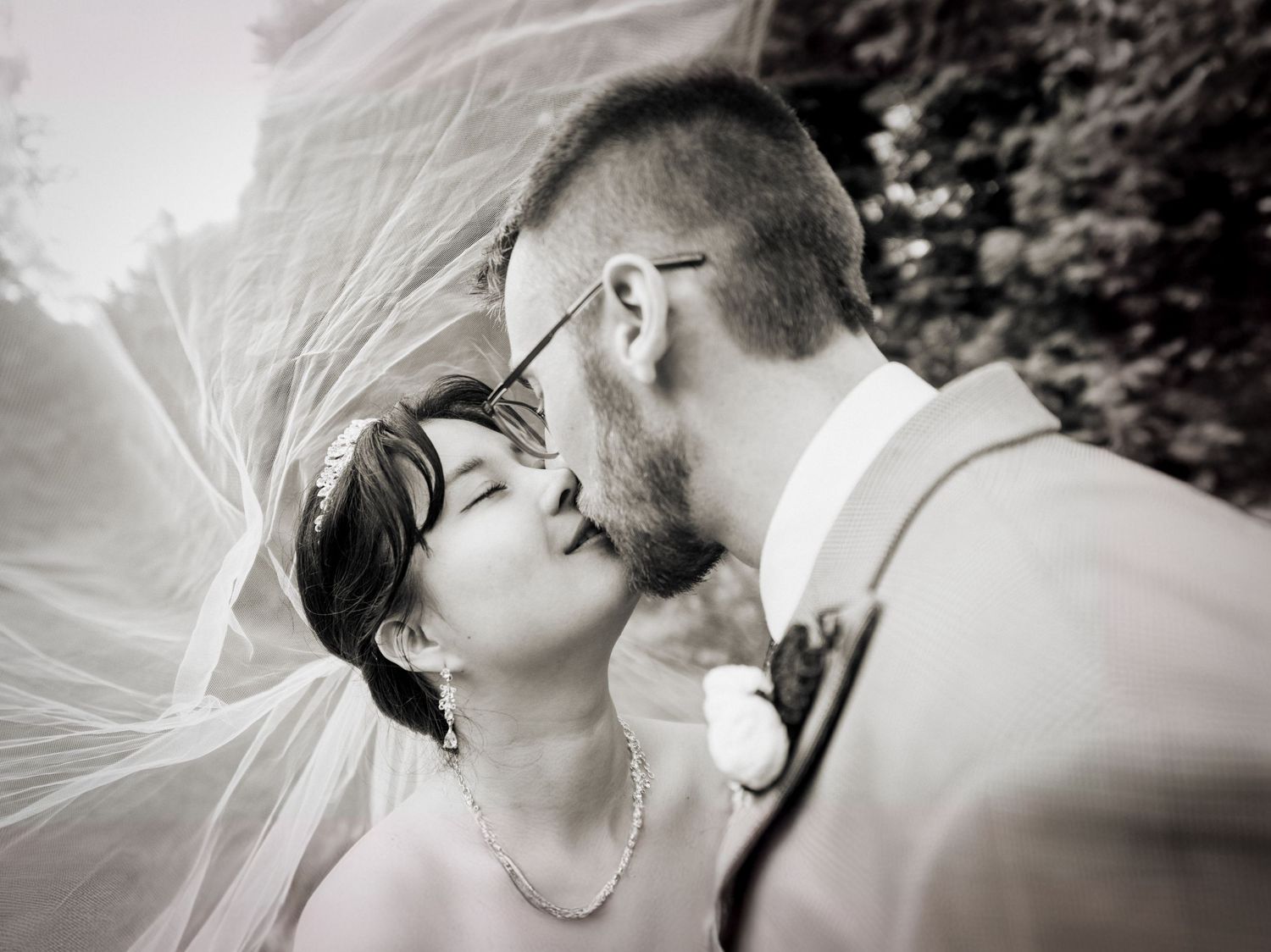 Black and white romantic wedding portrait with flowing veil in natural setting.