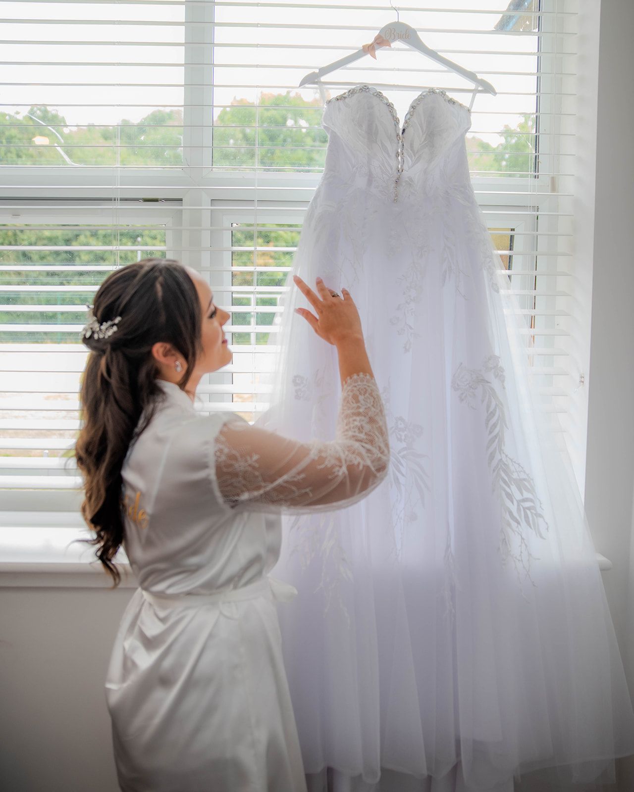 A series of images showing a white wedding dress being prepared and hung by a window.