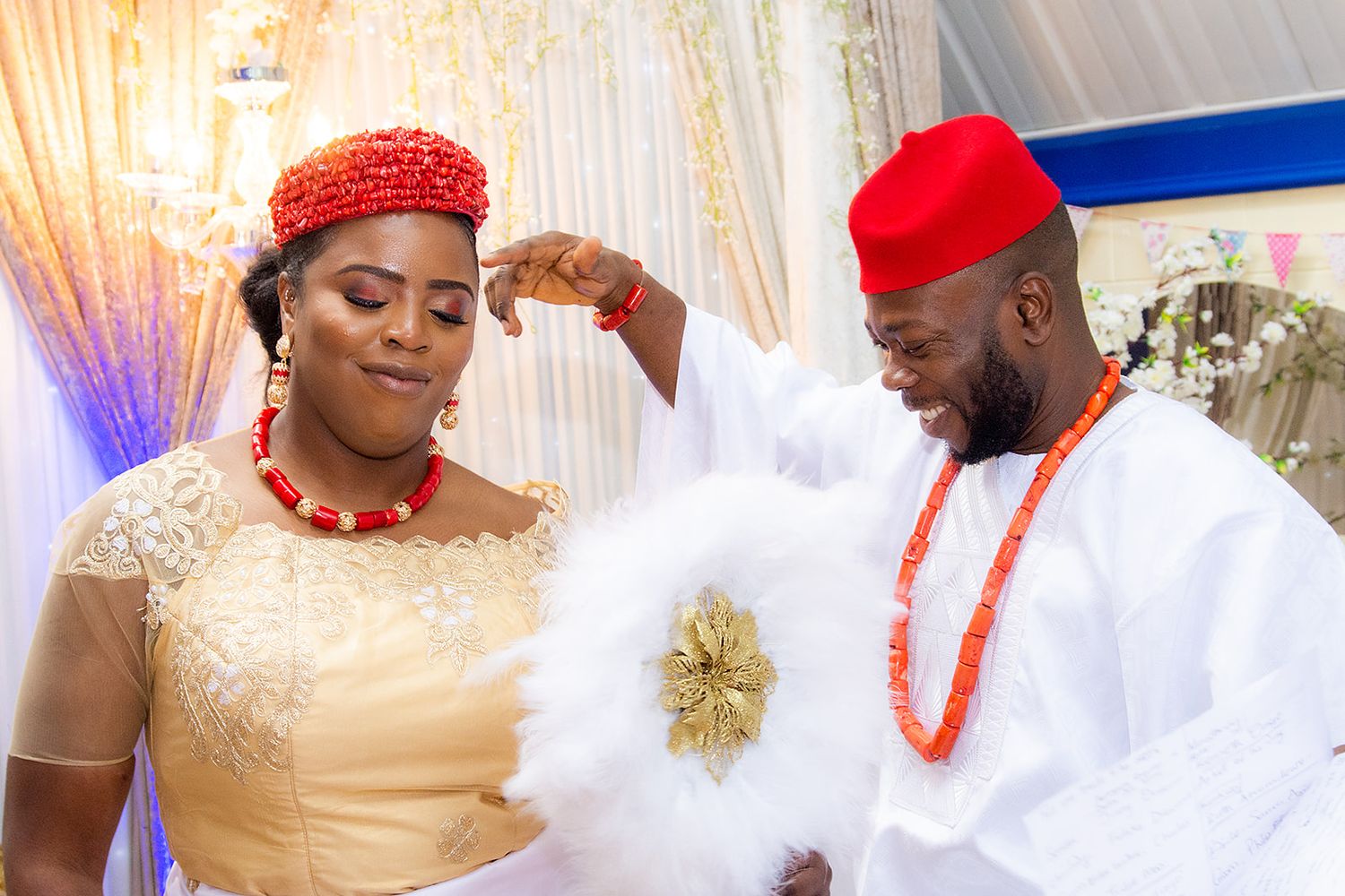 Traditional Nigerian wedding ceremony with guests in white and coral traditional attire.