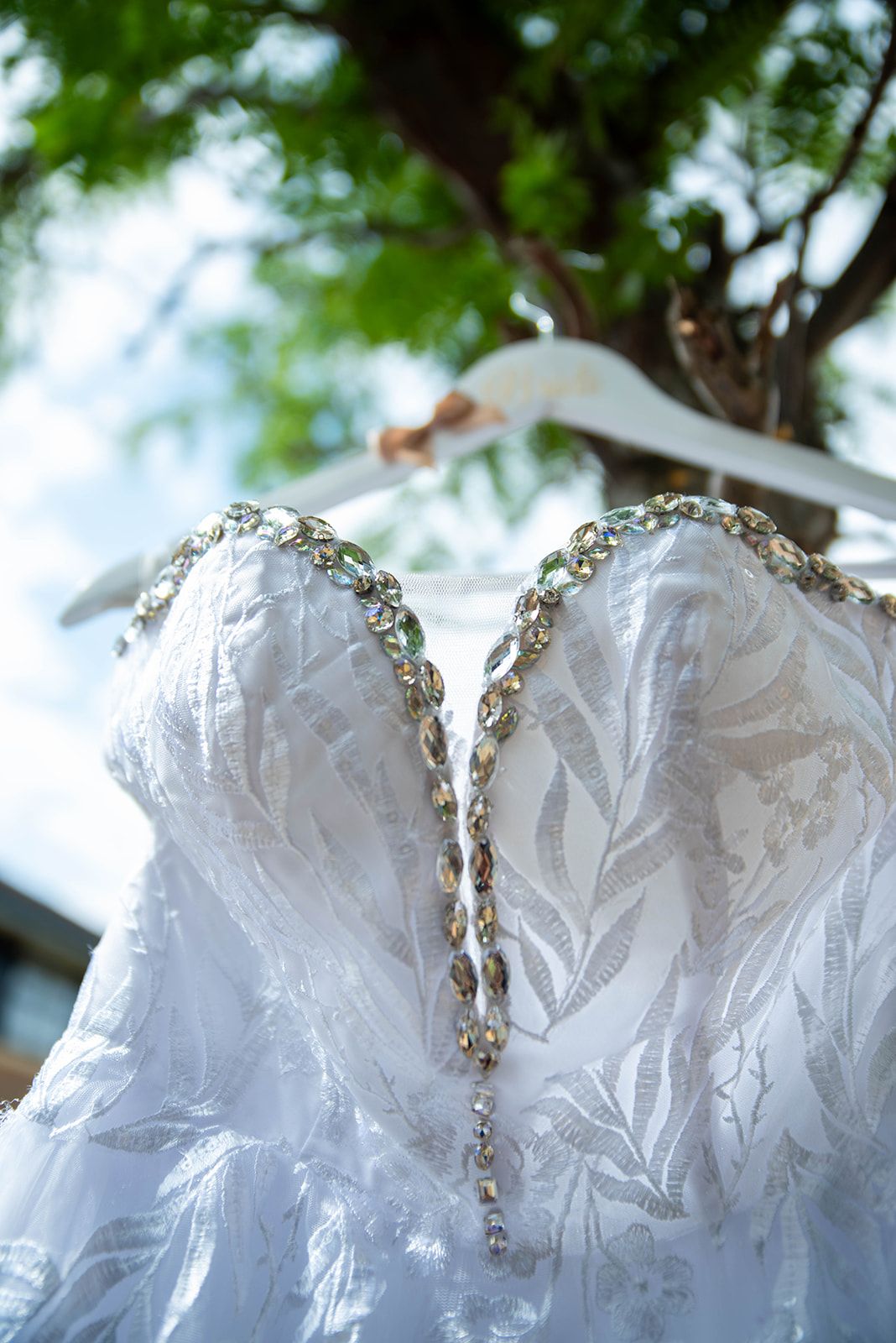 Close-up of white wedding dress bodice with crystal details hanging outdoors.