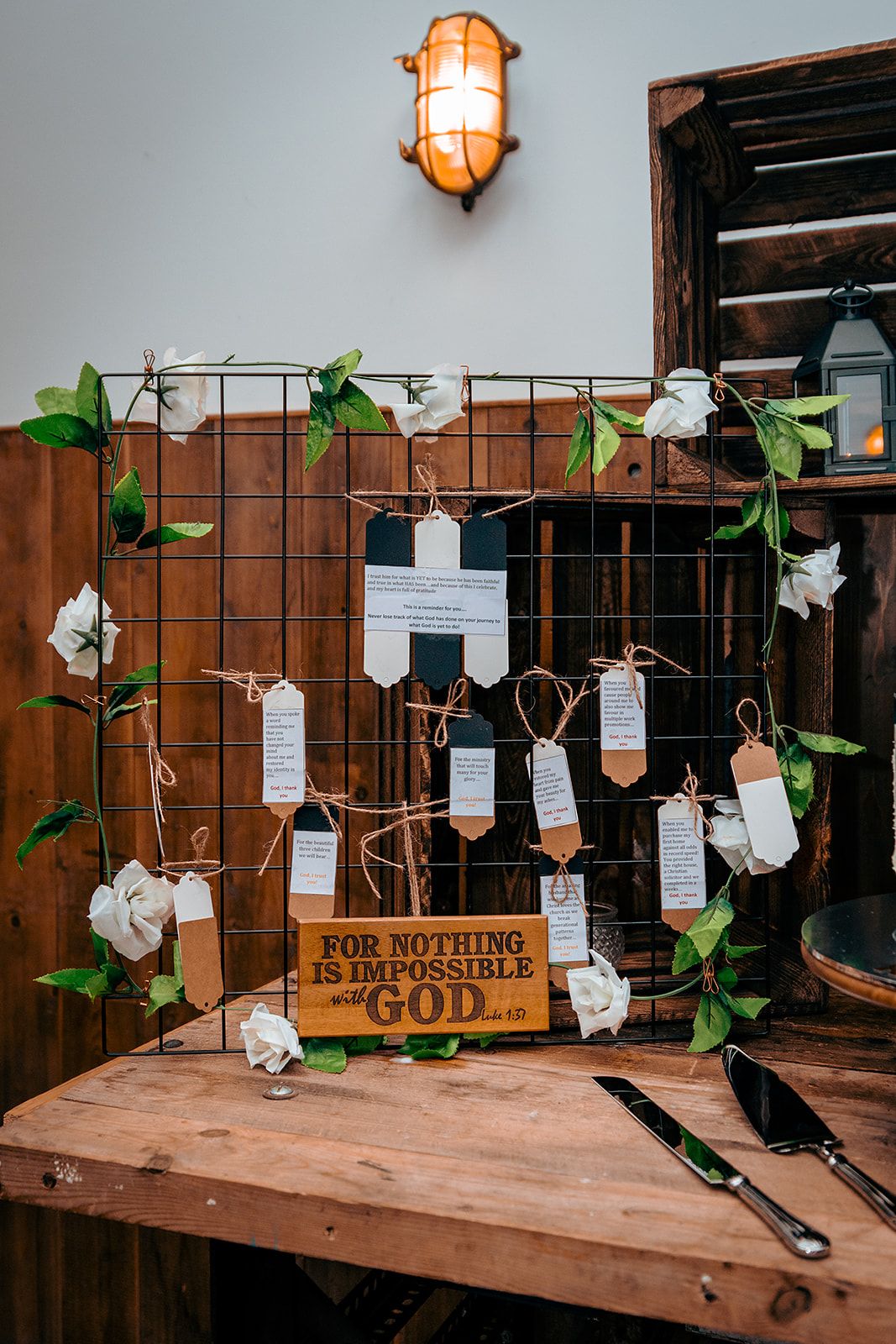 Rustic wedding seating chart display with hanging cards and greenery on wooden wall.