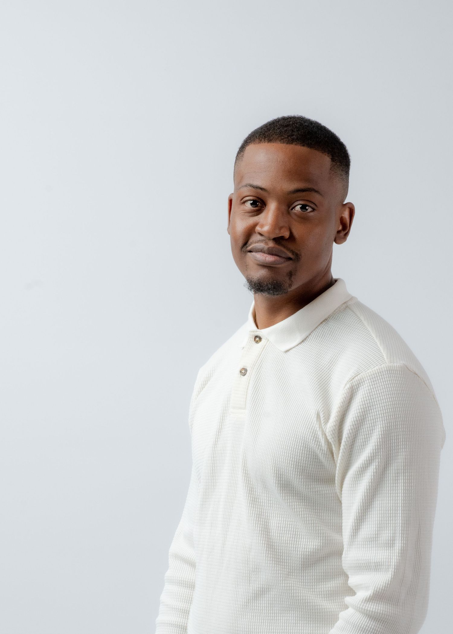 Studio portrait of a person wearing a white knit polo against a white backdrop.