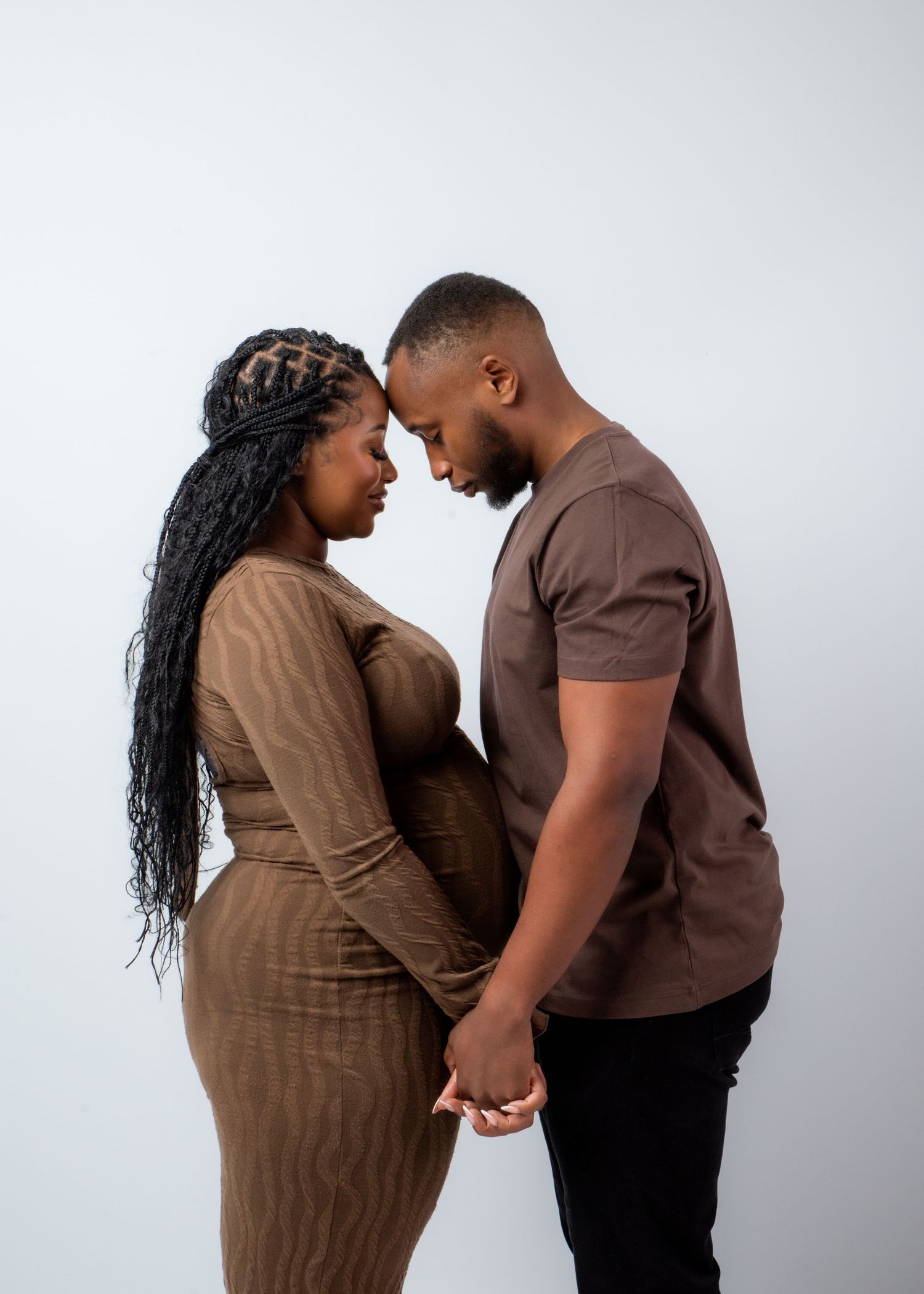 A couple in brown and black outfits shares an intimate moment in a series of romantic poses against a light background.