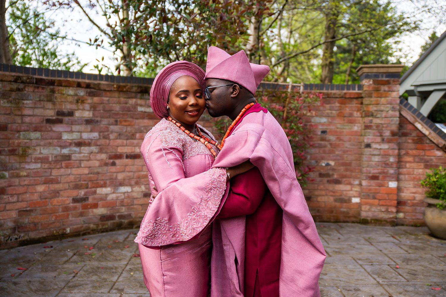 Wedding guests in pink and burgundy traditional African attire embracing outdoors.