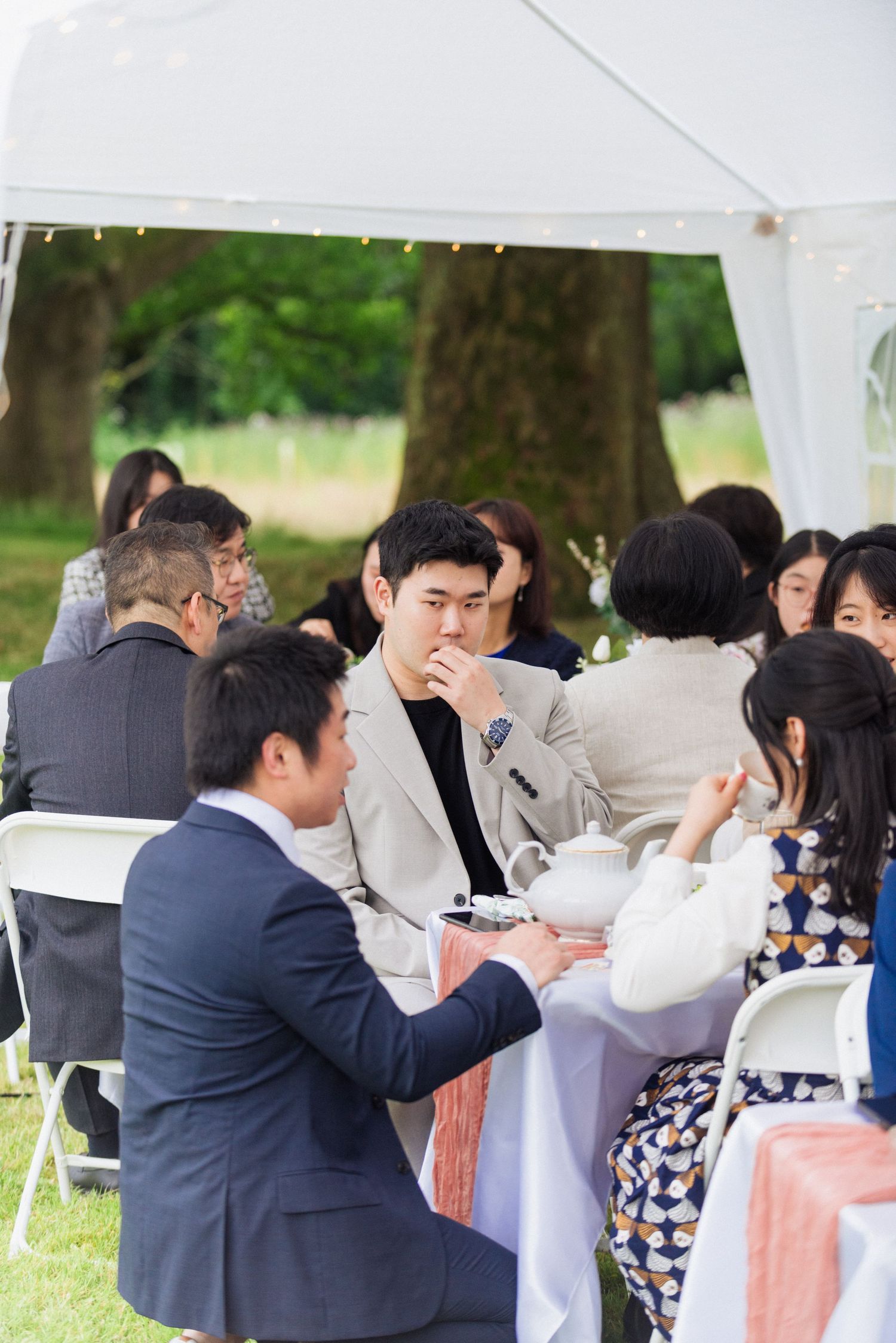 Wedding guests mingling under a white tent during an outdoor reception.