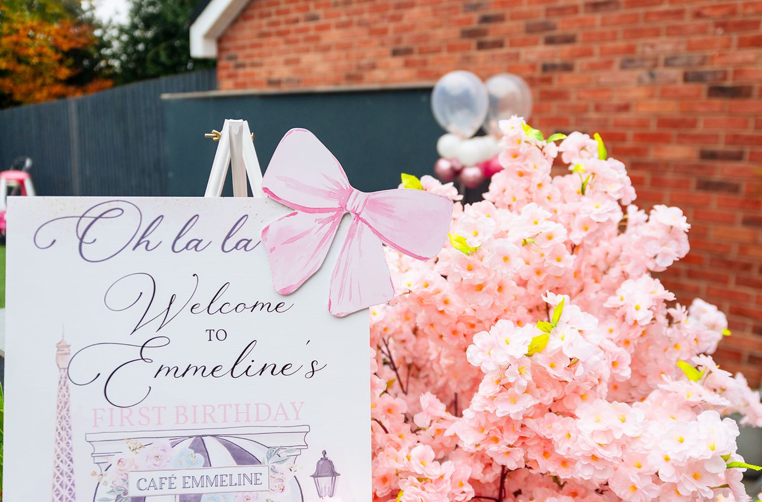 Outdoor party setup with pink floral decorations and brick building backdrop.