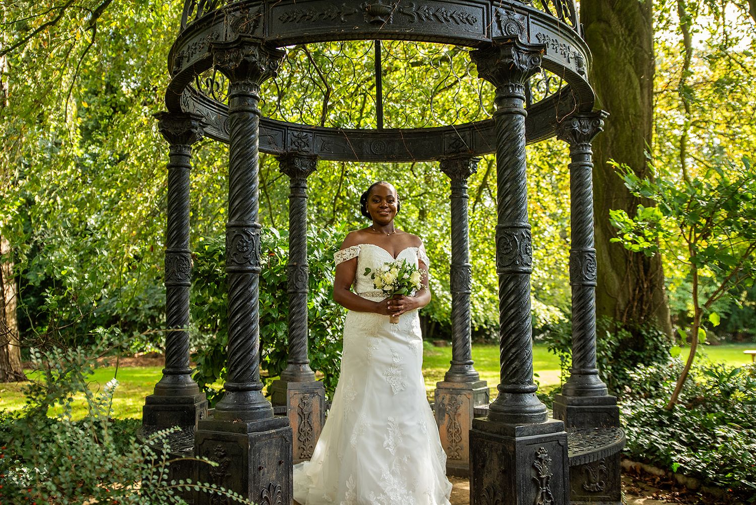 An elegant bridal portrait under a Victorian-style black iron gazebo surrounded by greenery.