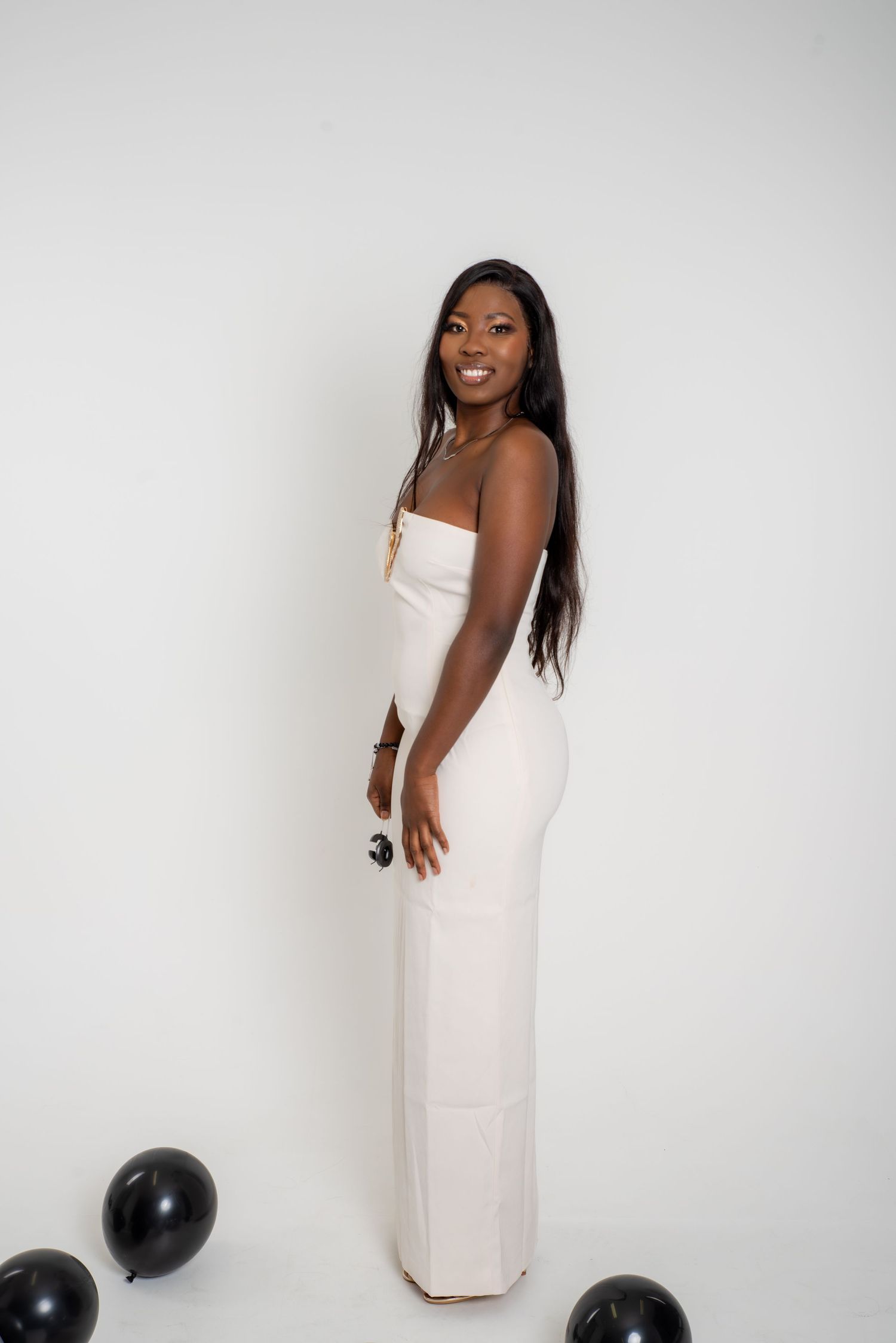A person in an elegant white dress poses with black balloons against a light background.