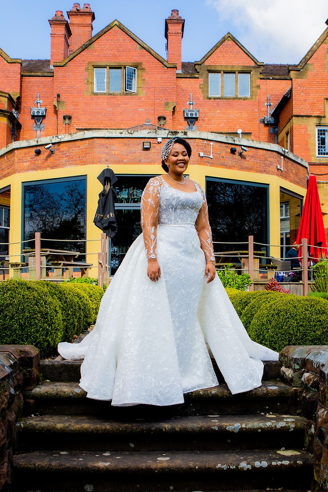 A bride poses in an elegant white wedding gown against a brick building backdrop.