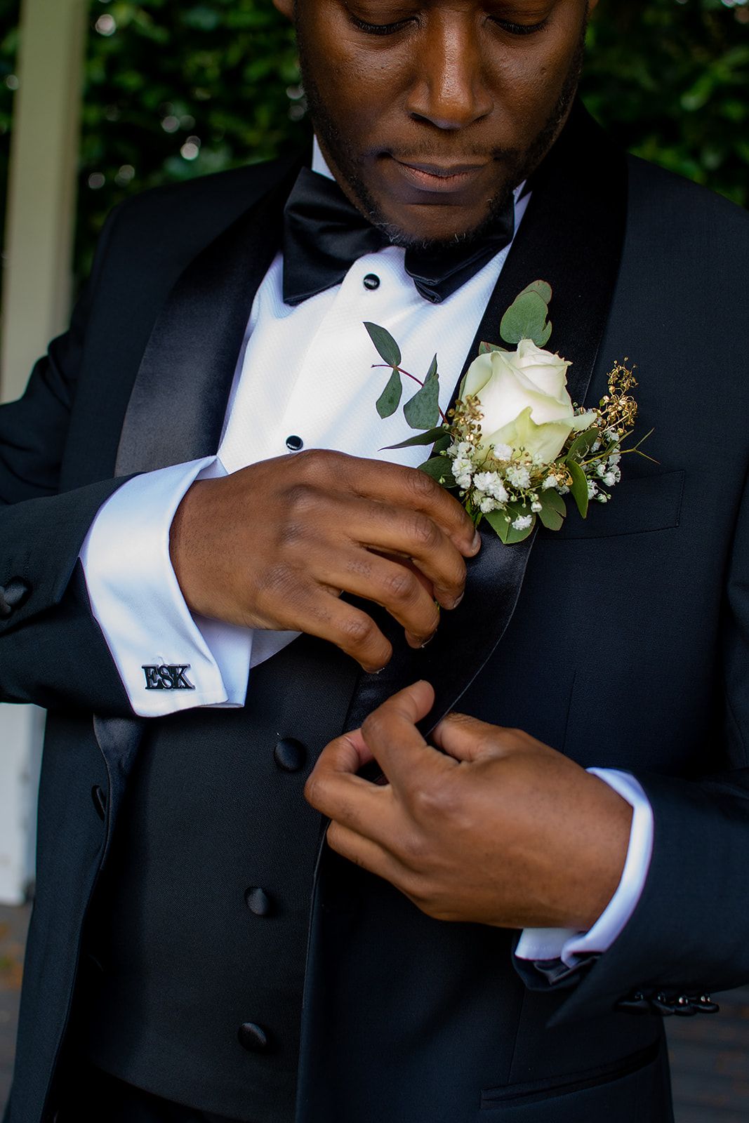 A close-up shot of a groom's boutonniere with a white rose against a black tuxedo.