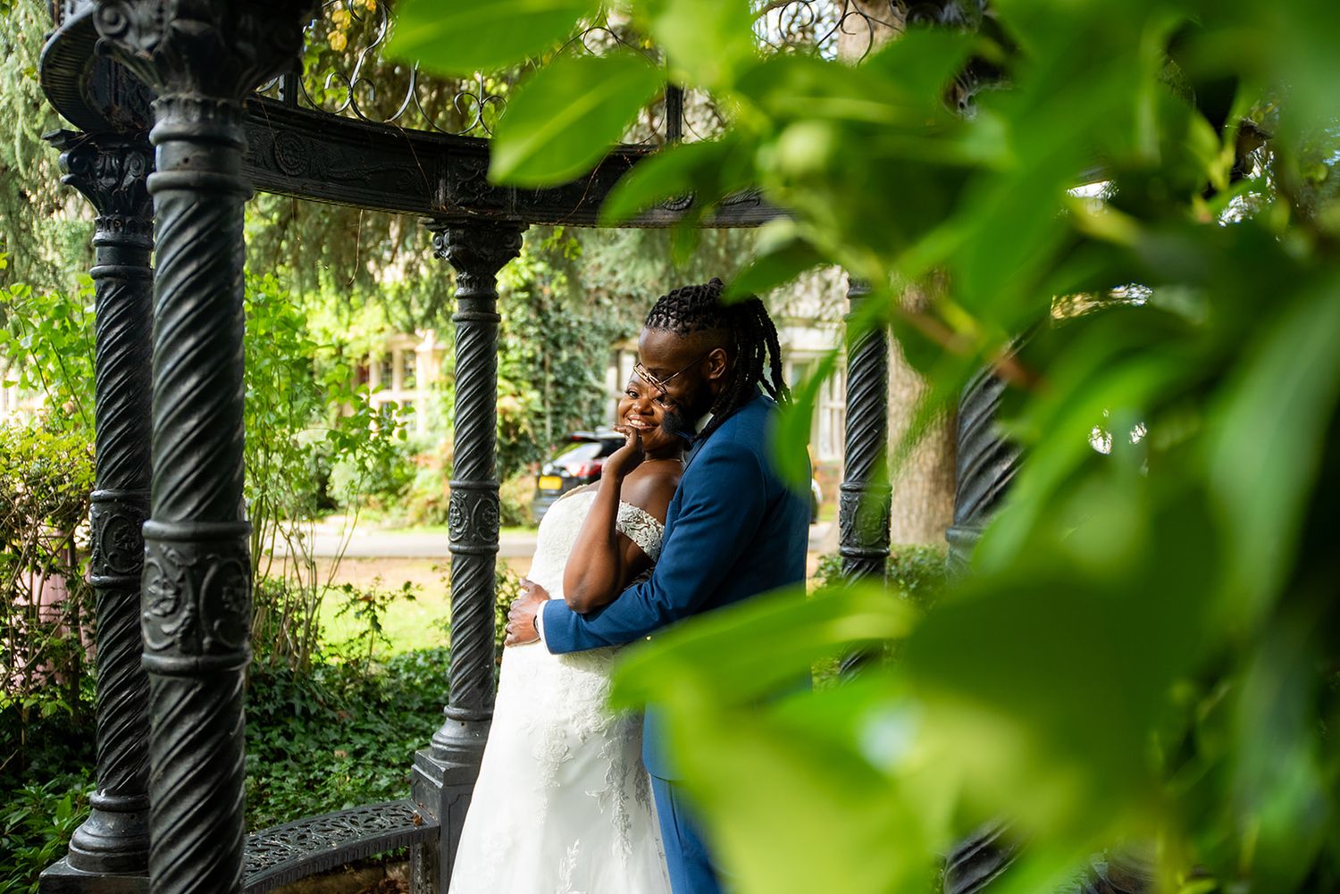 Wedding ceremony setting under a garden pergola with green leafy backdrop.