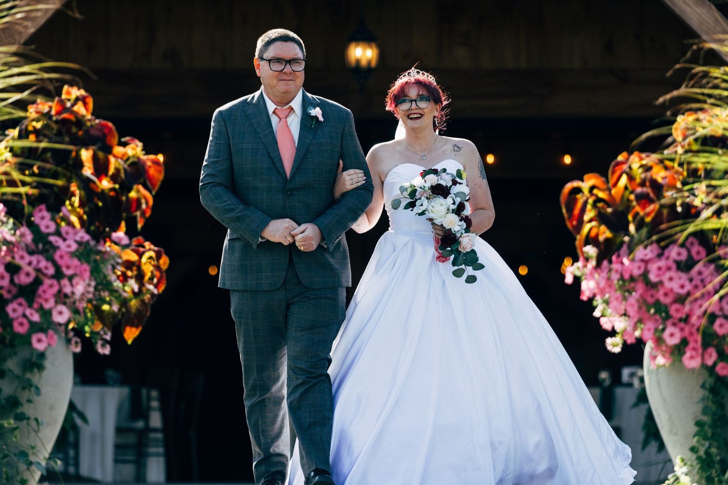 Bride in white ball gown walks down the aisle with her father at an outdoor wedding ceremony.