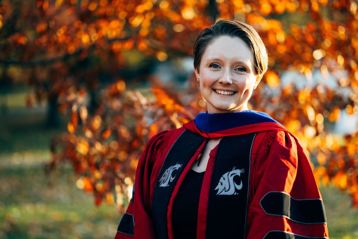Autumn portrait session with vibrant orange foliage and sunlit bokeh in the background.