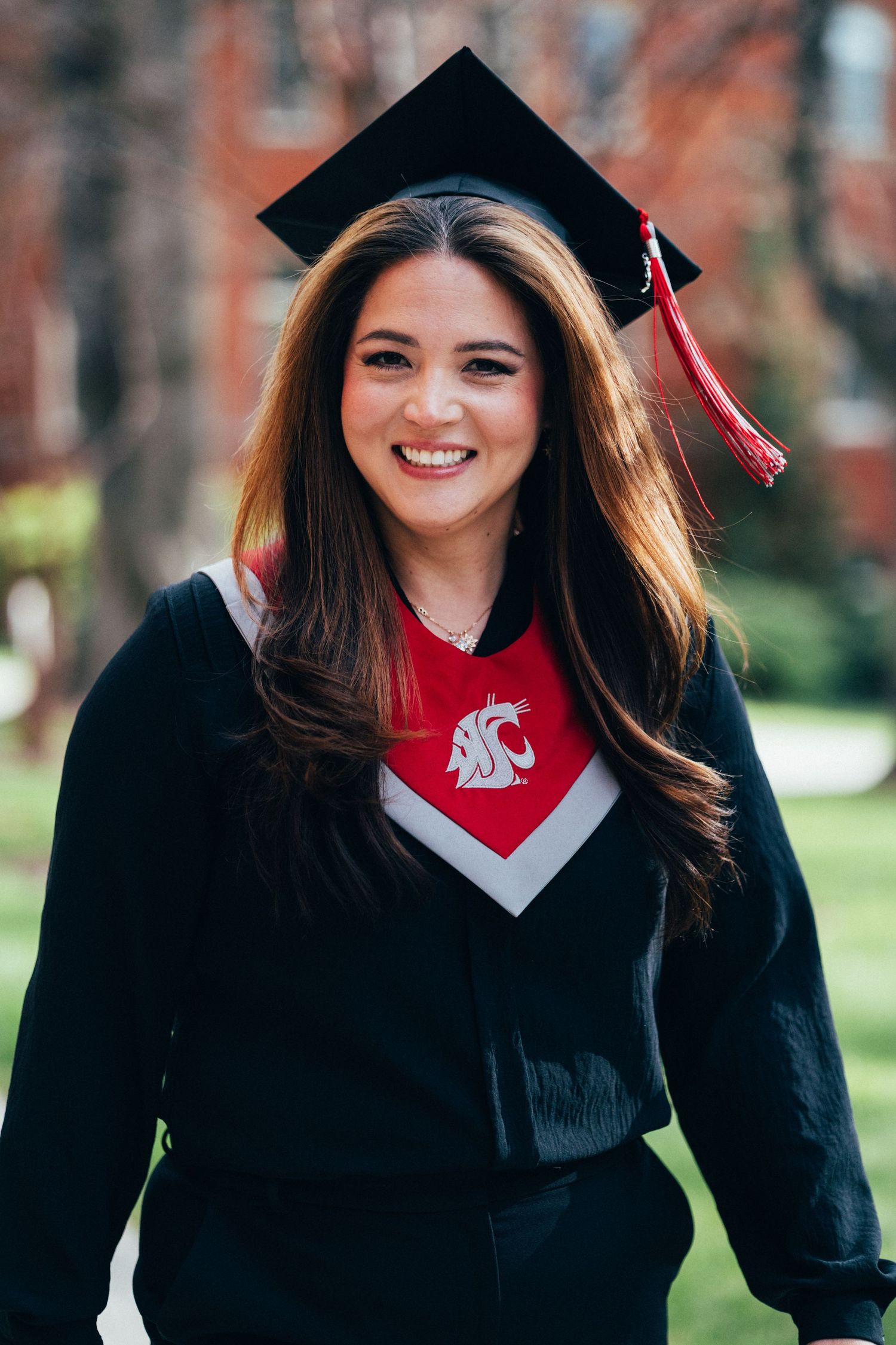 Smiling young woman in black graduation cap and gown wearing a Washington State University shirt outdoors.