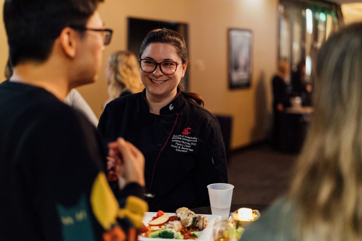 People gathered at a social event enjoying food and drinks in a warmly lit venue.