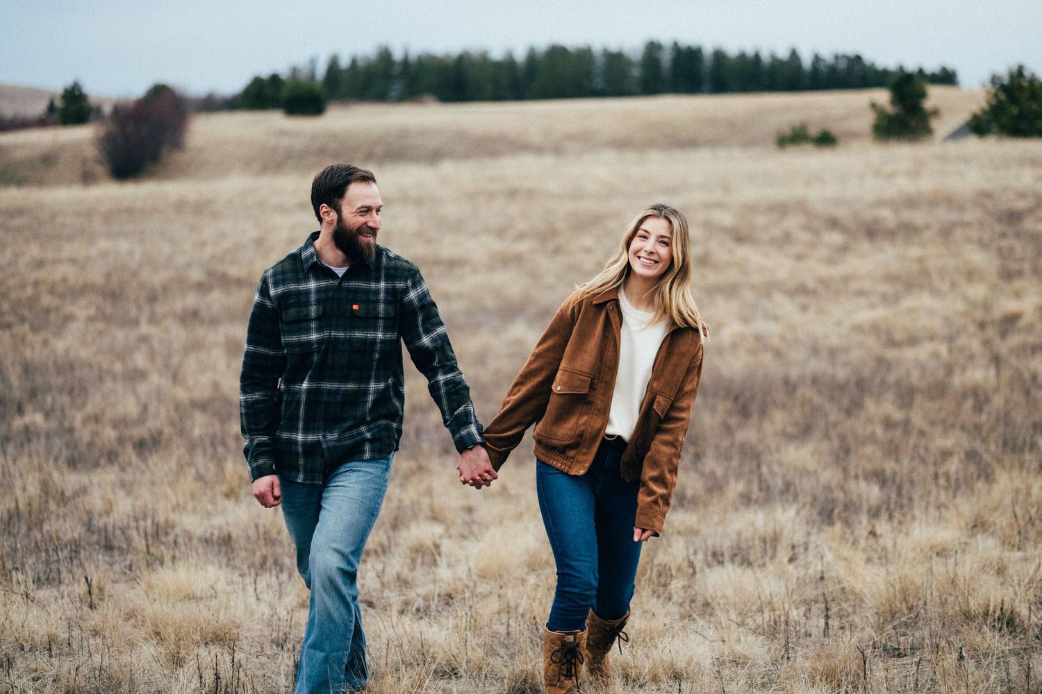 Couple walking through golden field during rustic outdoor photo session.