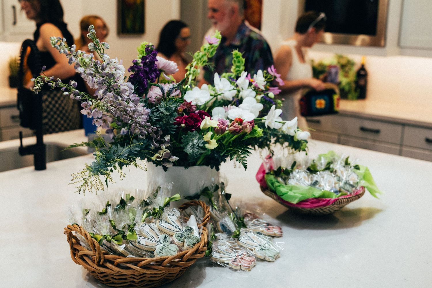 Elegant floral arrangements in wicker baskets and vases displayed on a white counter at an indoor event.