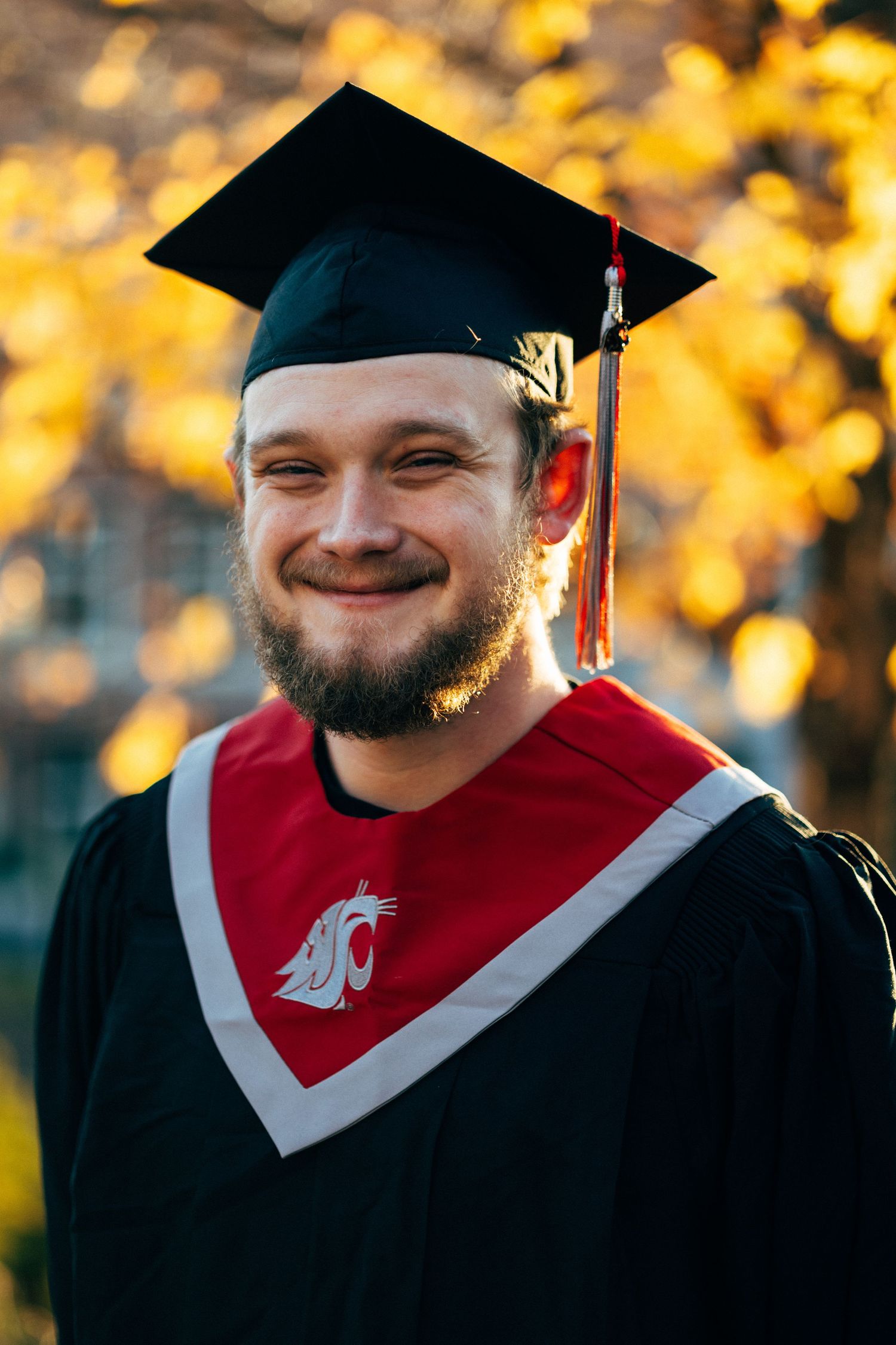 Graduate in WSU regalia smiling during sunset graduation photos.