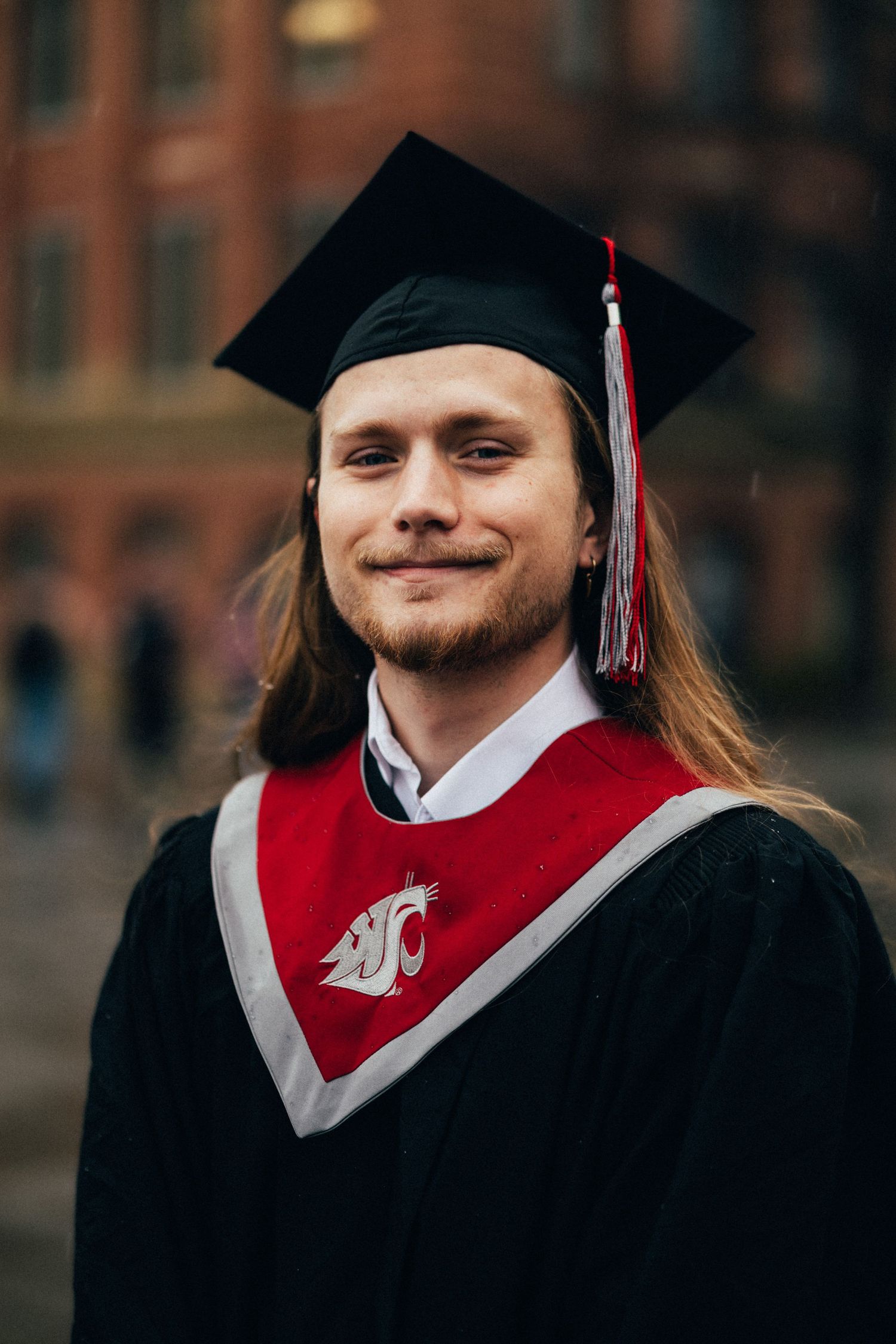 Graduate wearing red and black academic regalia smiles during commencement ceremony.