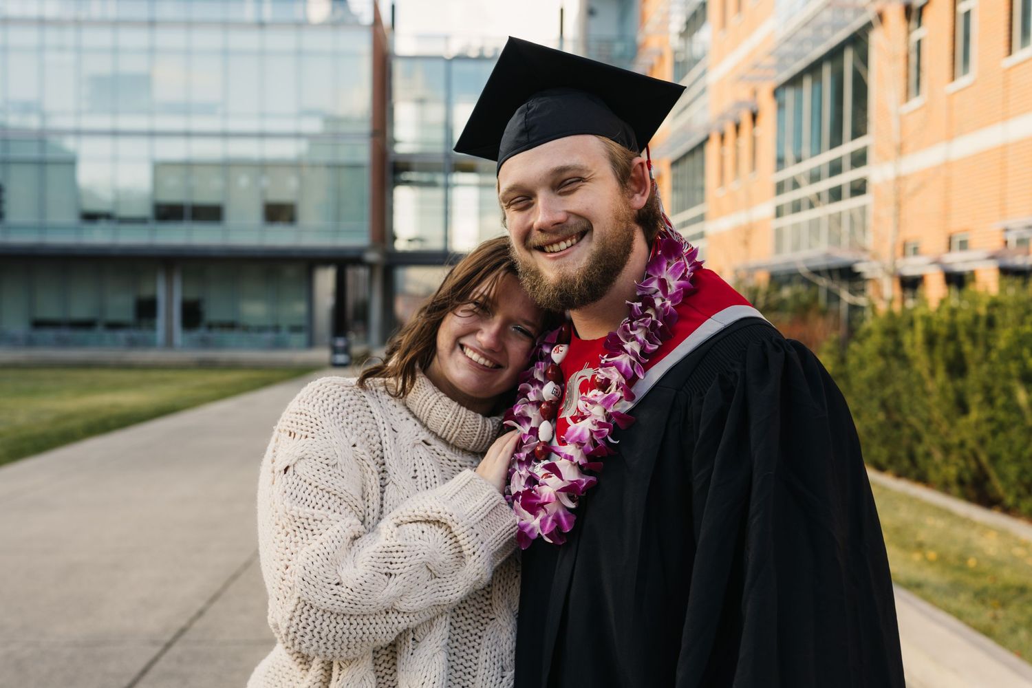 A graduate in cap and gown celebrates with loved one outside a campus building.