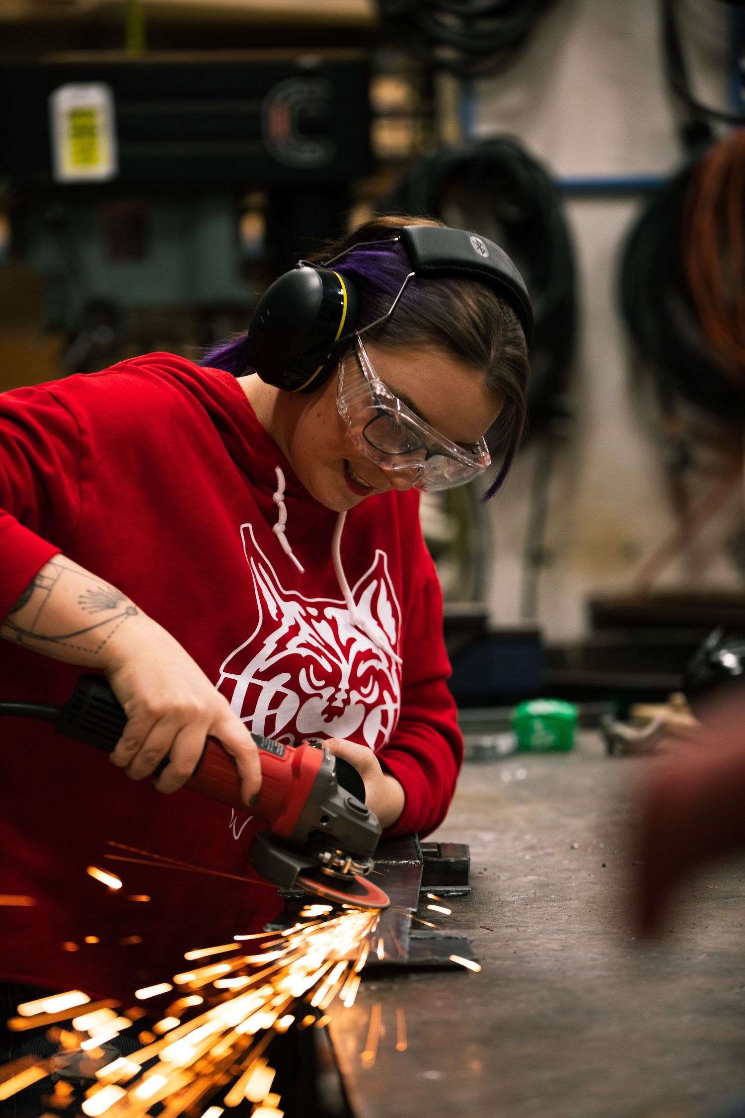 Sparks flying from metal grinding in workshop with person in red shirt.