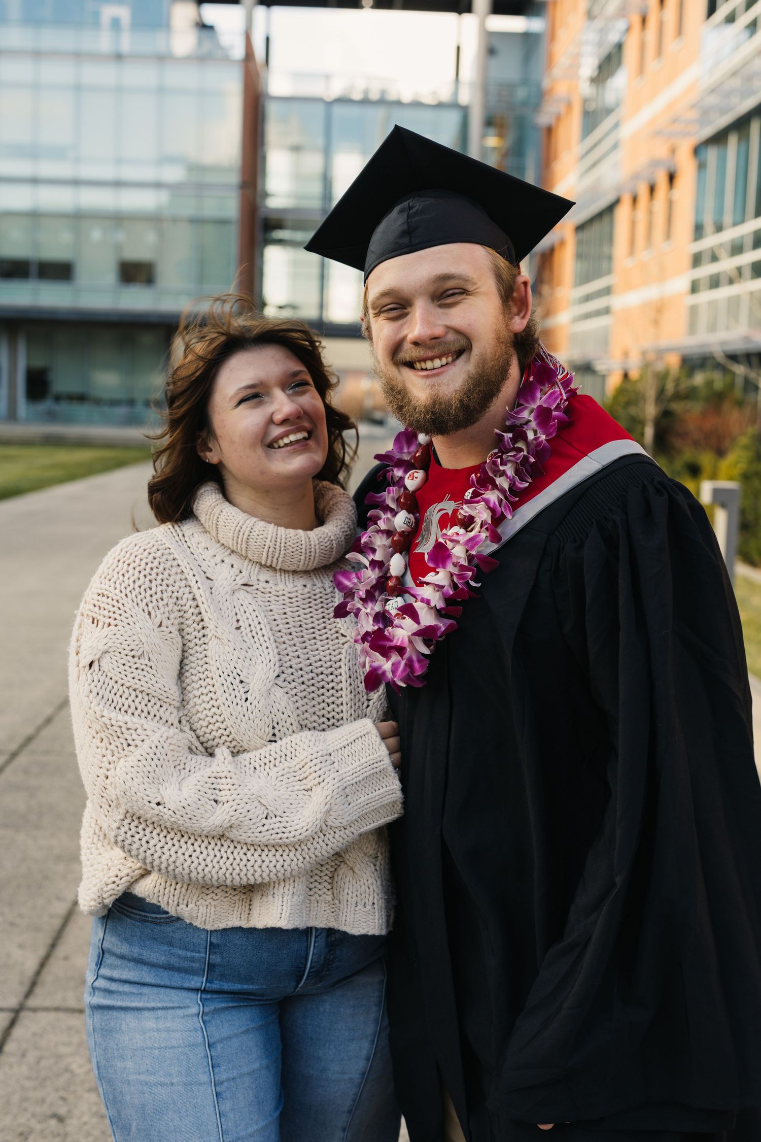 A graduation celebration outdoors with a graduate wearing a cap, gown and purple lei.