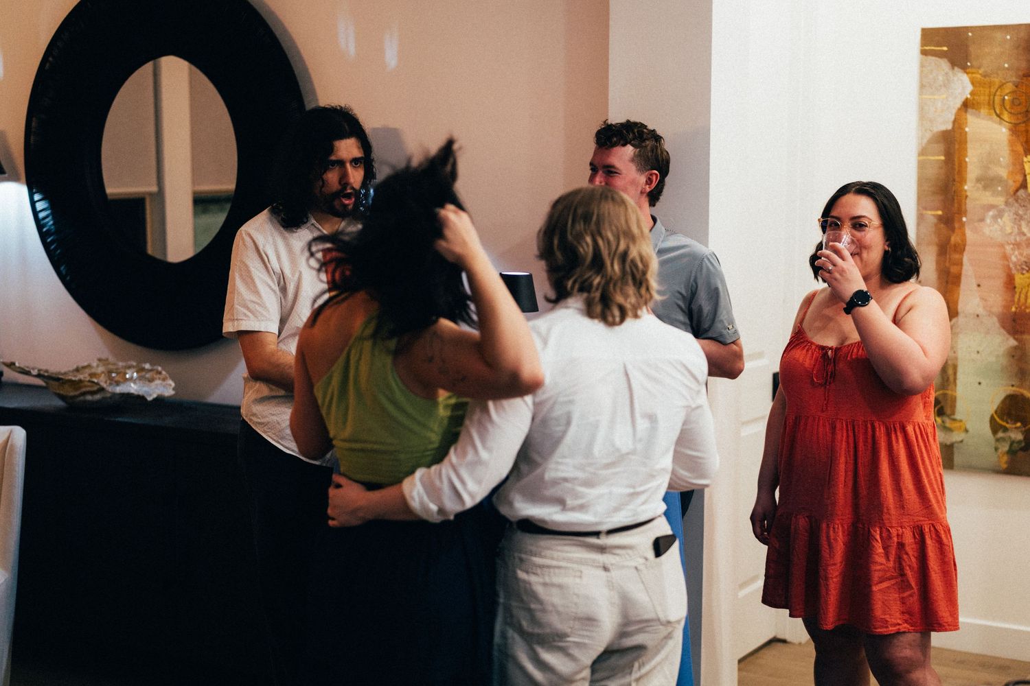 Group of people socializing at an art gallery opening, wearing casual summer attire in a bright modern space.