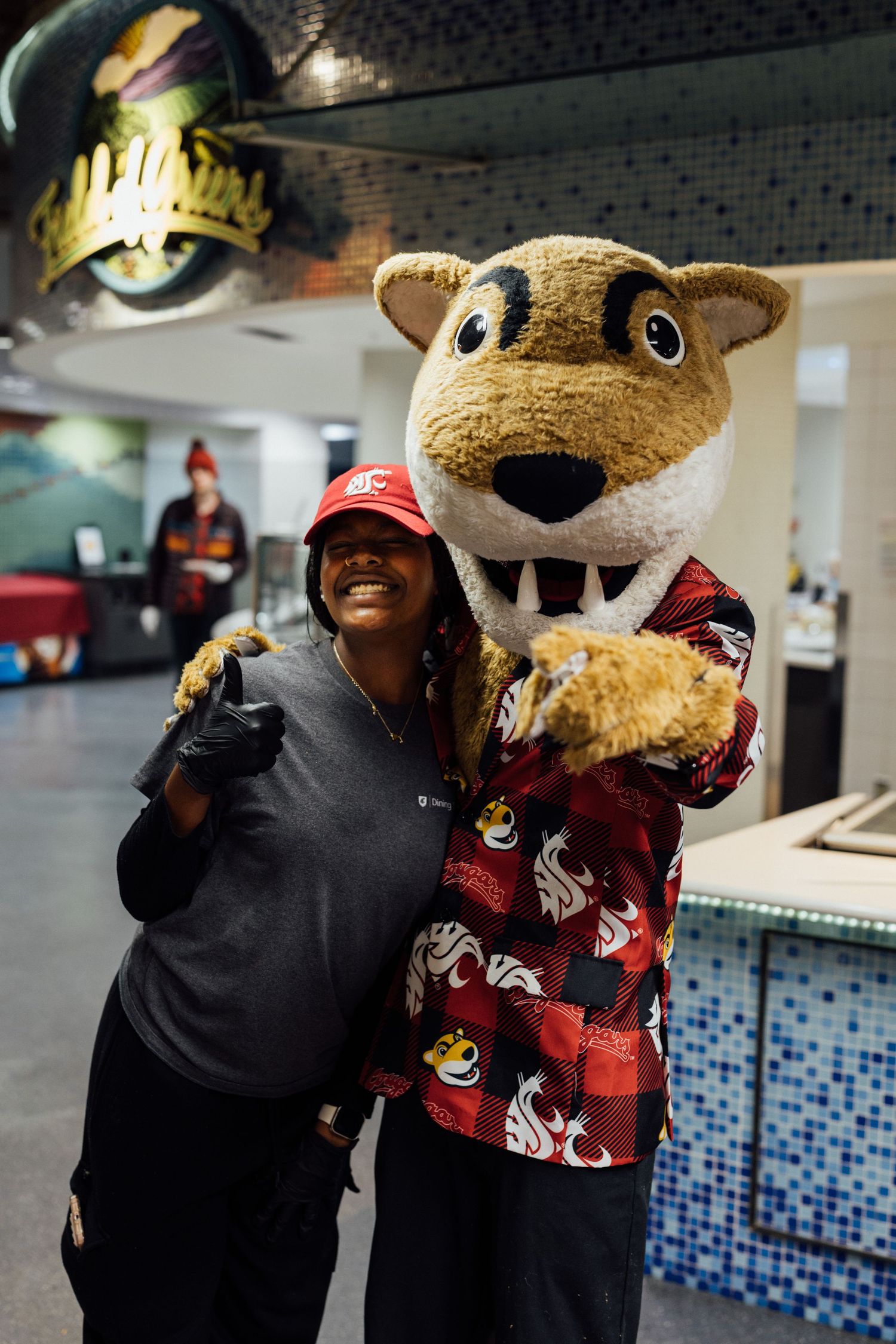 A mascot in a furry brown costume interacts playfully with staff members wearing red uniforms.