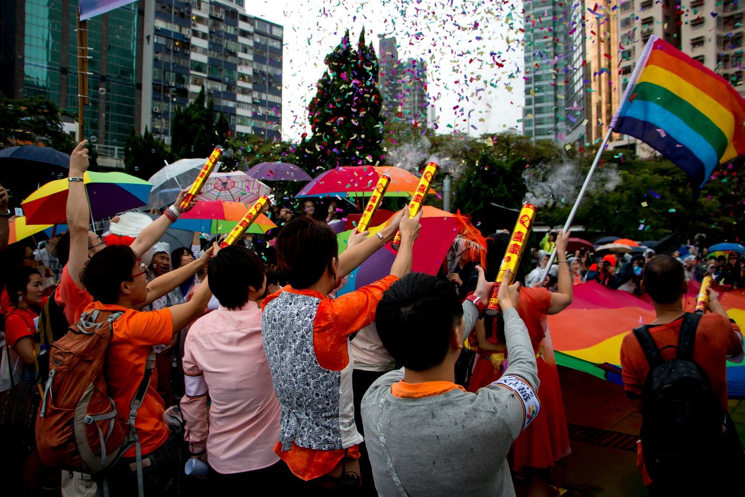 Crowd celebrating with rainbow flags and confetti at an outdoor urban event.