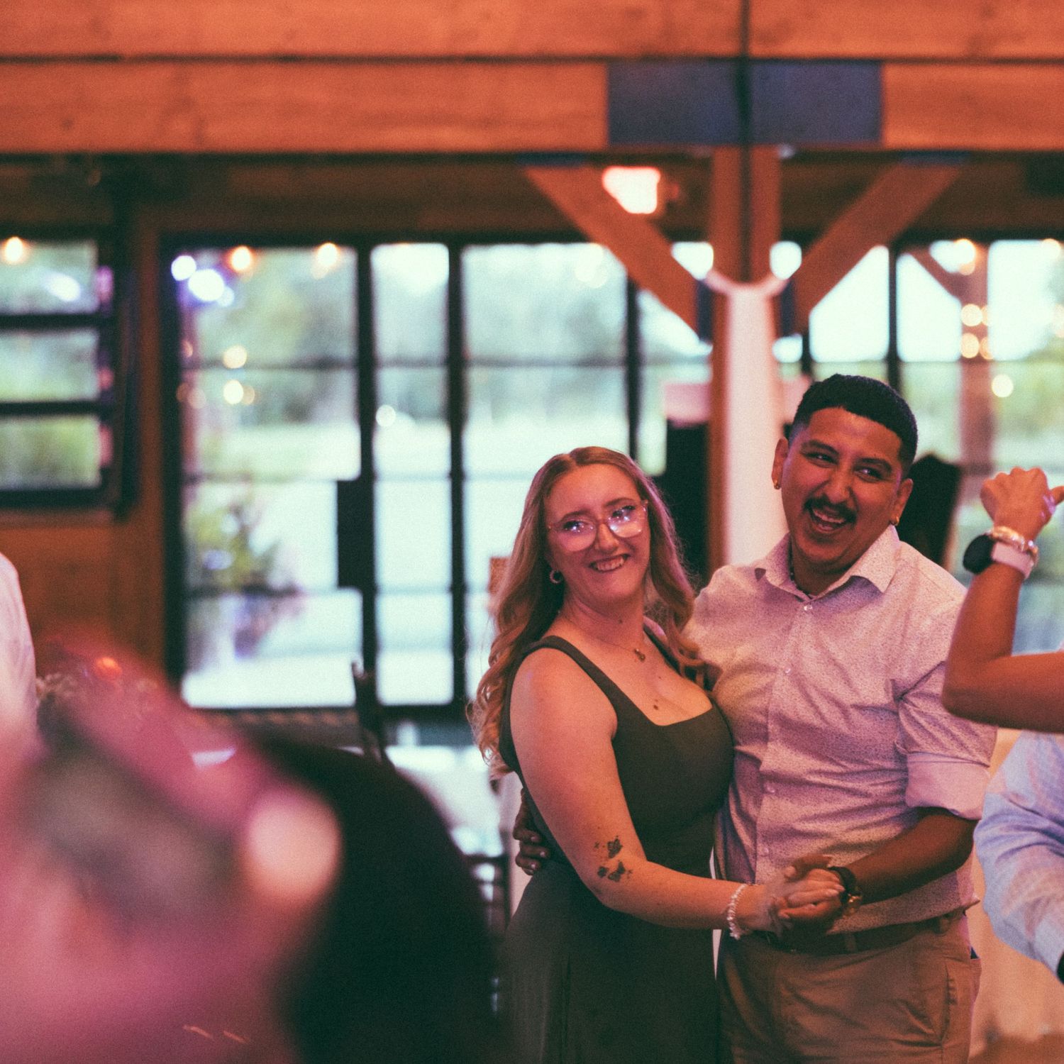 A smiling couple poses together at an indoor event venue with warm lighting and large windows in the background.