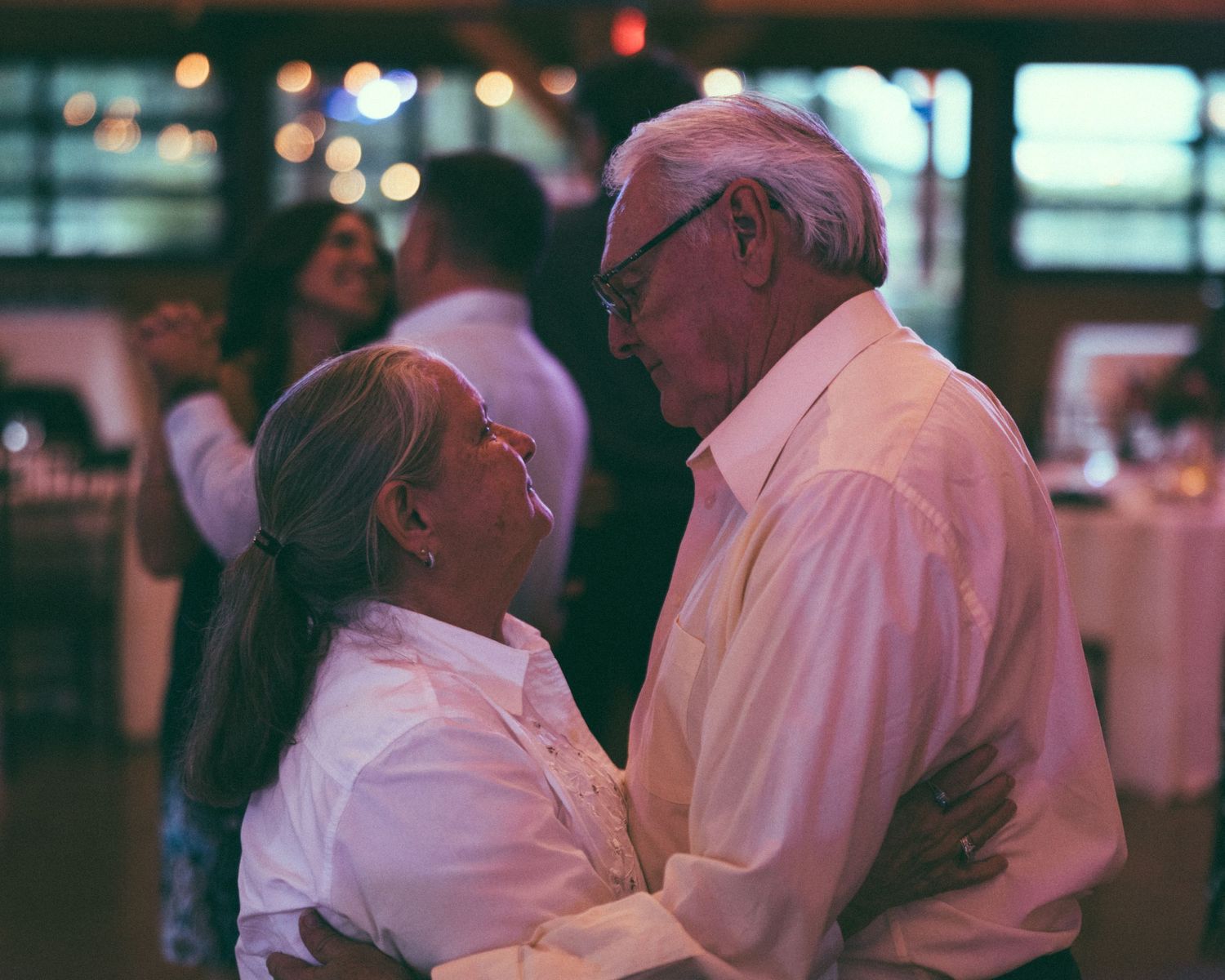 Elderly couple sharing a romantic dance at a wedding reception in a warmly lit venue.