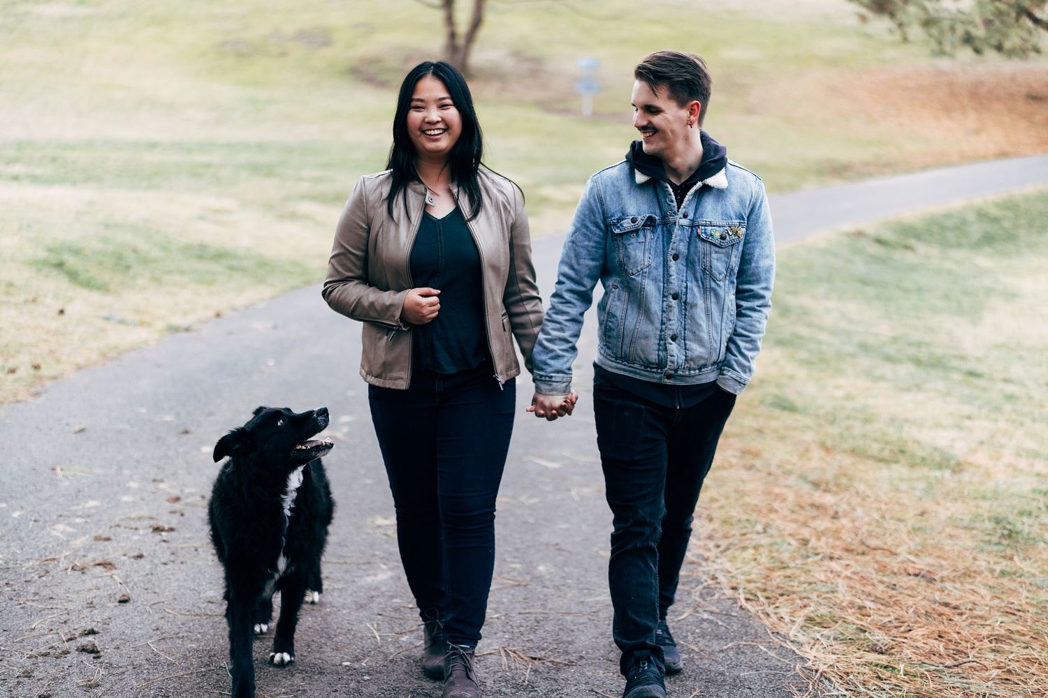 Couple walking on path with black dog in natural outdoor setting.