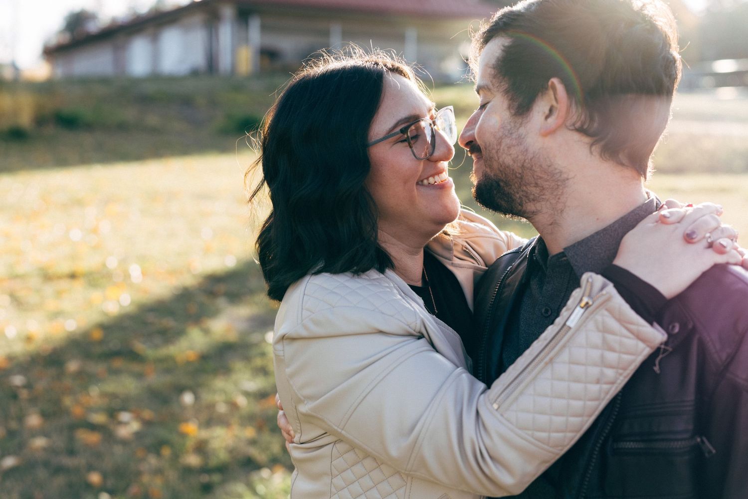 Couple embracing outdoors during golden hour with sunlit autumn foliage in background.