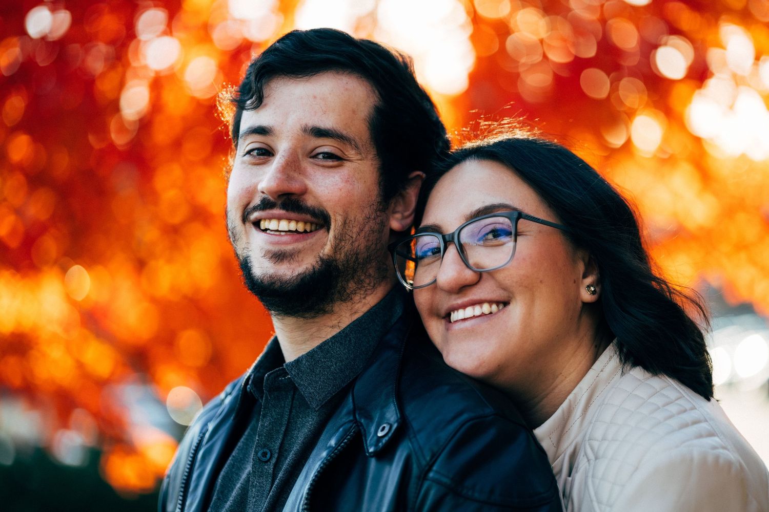 A couple embracing against a backdrop of vibrant orange autumn bokeh lights.