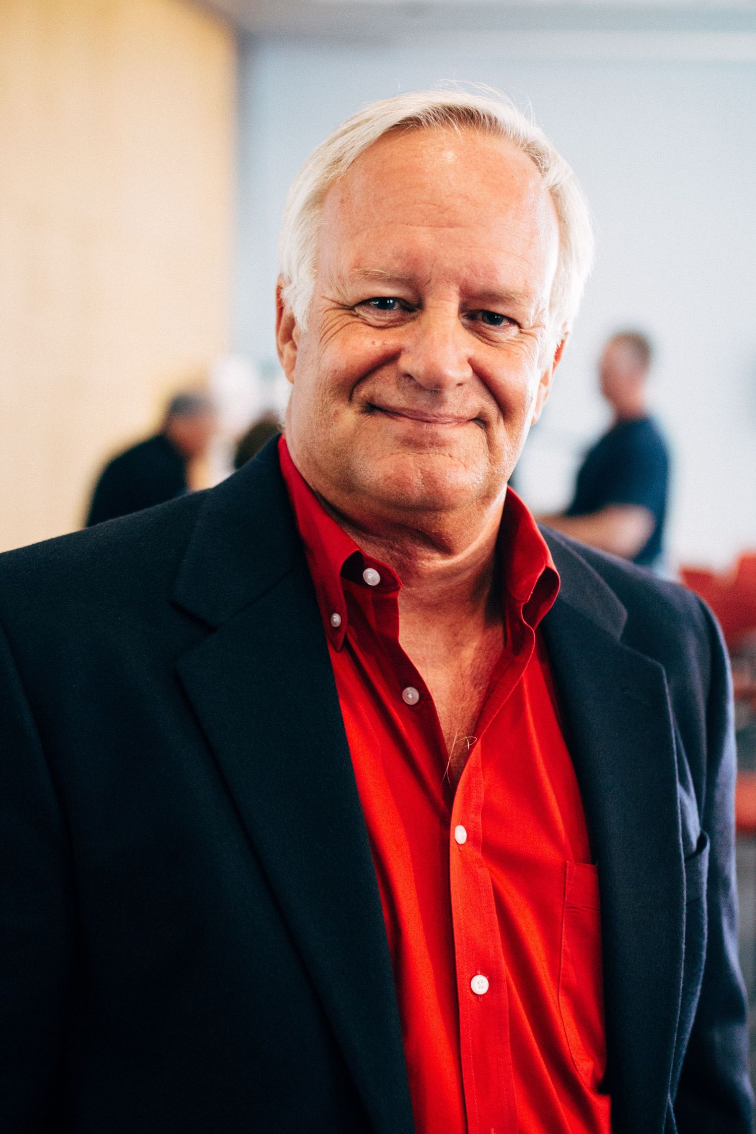 Person wearing a black blazer and red shirt in a formal indoor setting.
