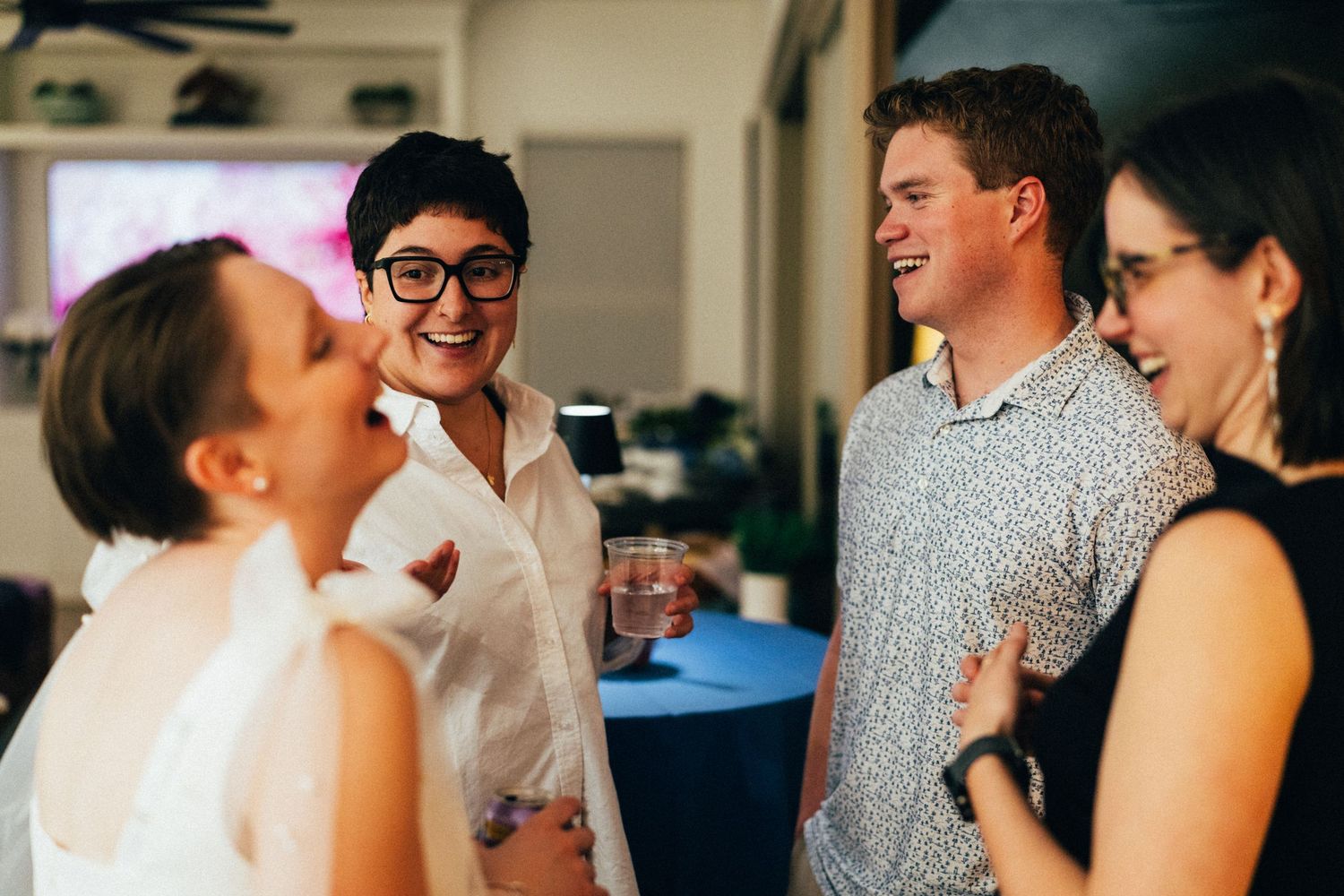 Four young adults laughing and socializing at an indoor party event.