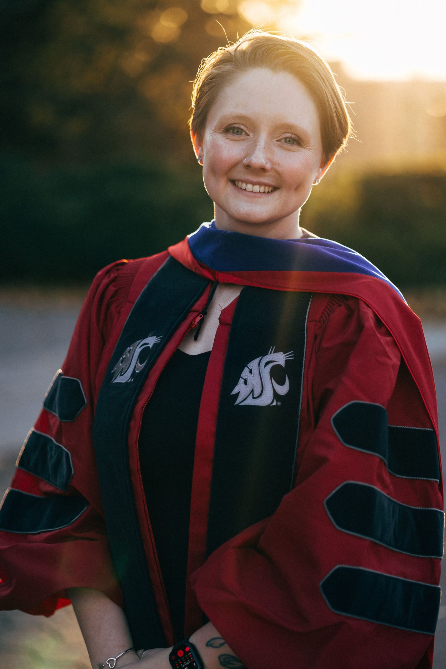 Graduate in crimson and black academic regalia photographed during golden hour.